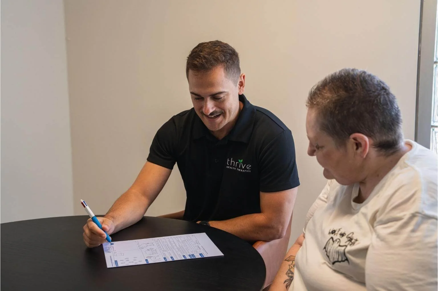 Occupational therapist and client sitting at table during assessment in the cumminty