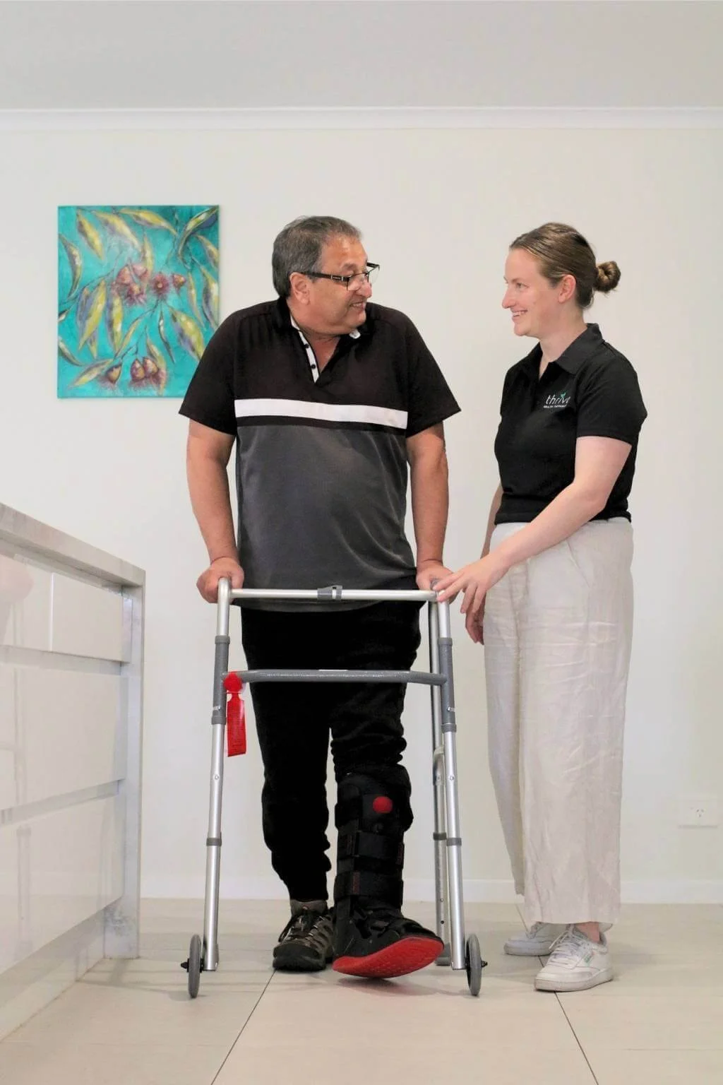 Occupational therapist assisting client who is using a walking frame at home during a home modifications assessment