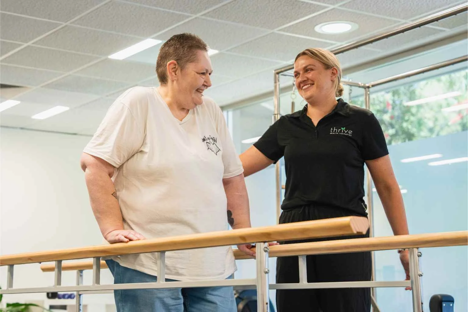Exercise physiologist assisting client who is using parallel bars during a session at the Thrive Health Therapies gym in Findon, Adelaide
