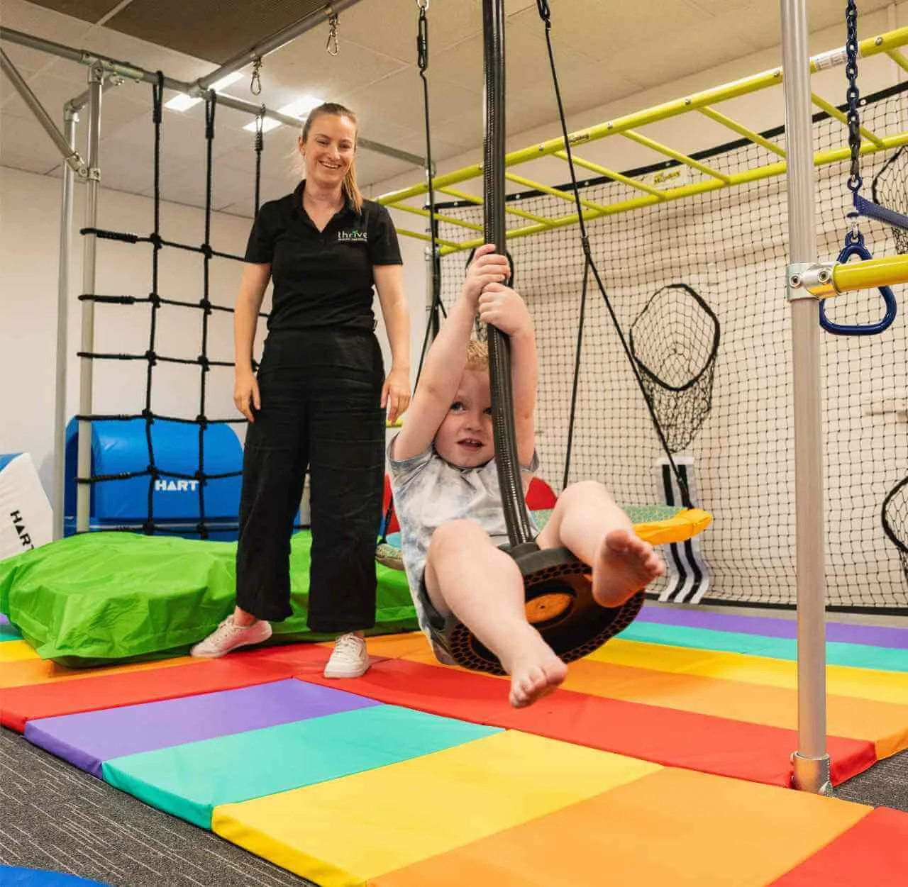 Young child swinging on equipment with therapist smiling in background at Thrive Health Therapies Findon clinic during occupational therapy session