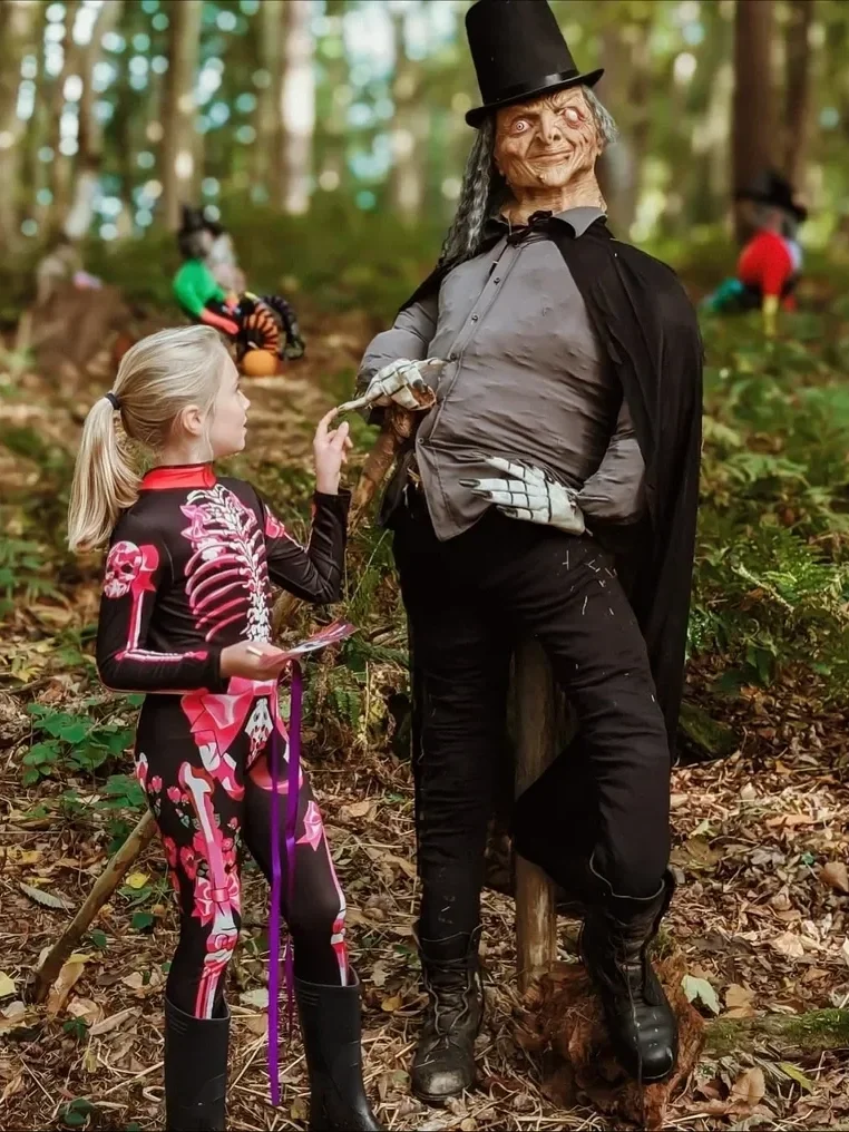 A girl dressed in a skeleton costume talking to a spooky witch figure in a forest during Halloween.