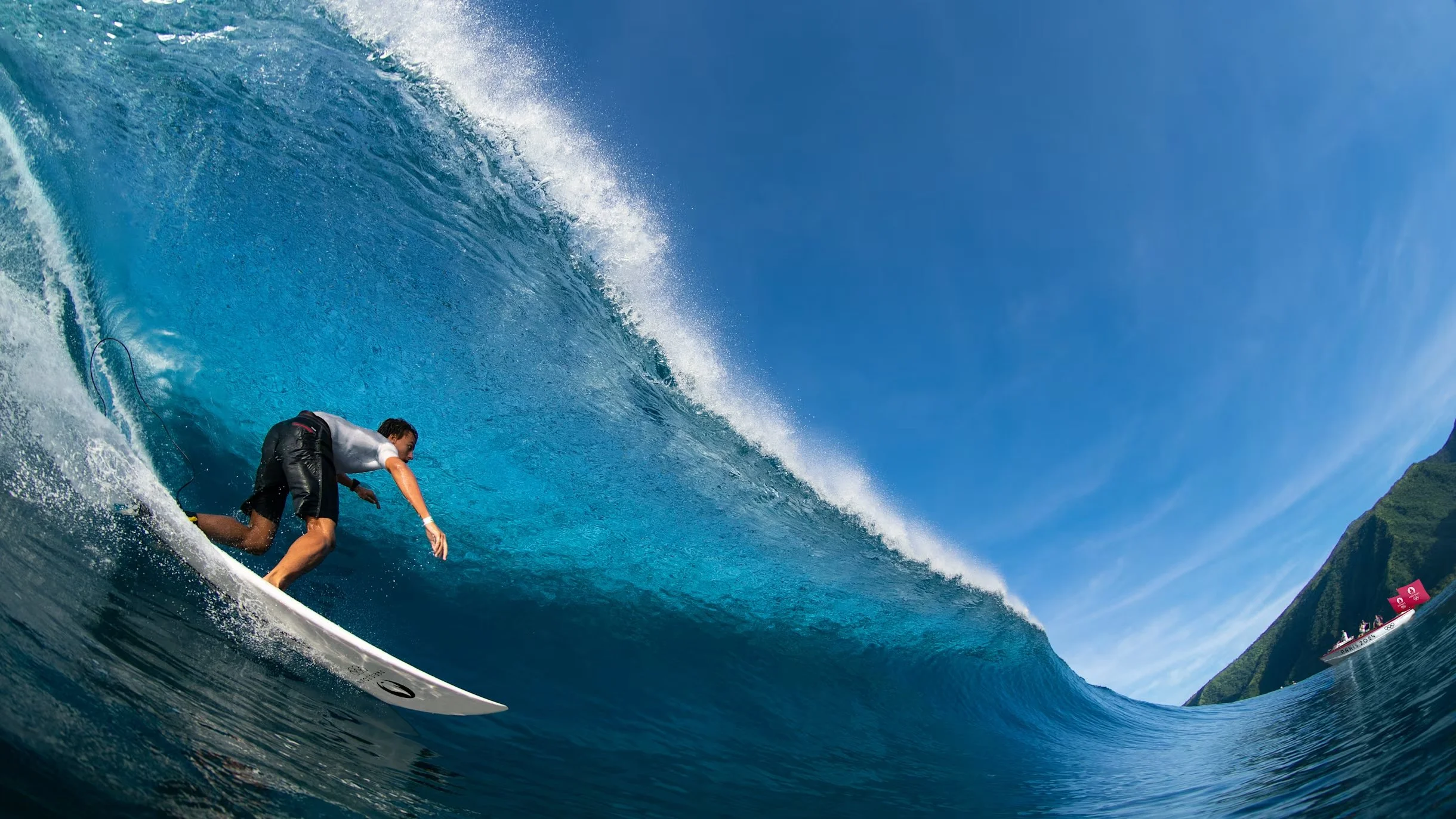Surfeur à l'intérieur d'une grosse vague dans l'océan avec une montagne et un bateau en arrière-plan