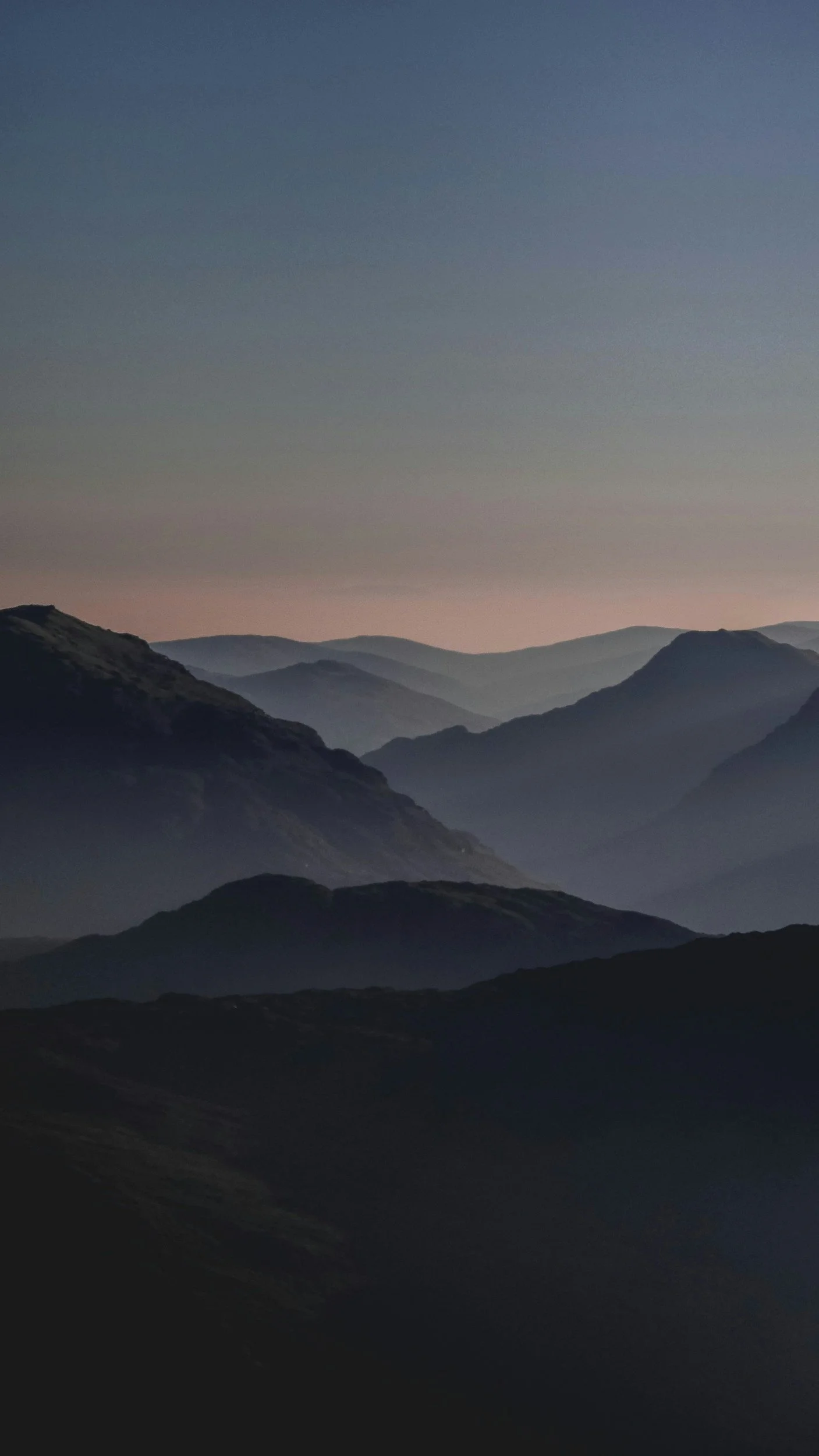 Layered mountain ranges in shades of blue and purple at dusk or dawn with a clear sky.
