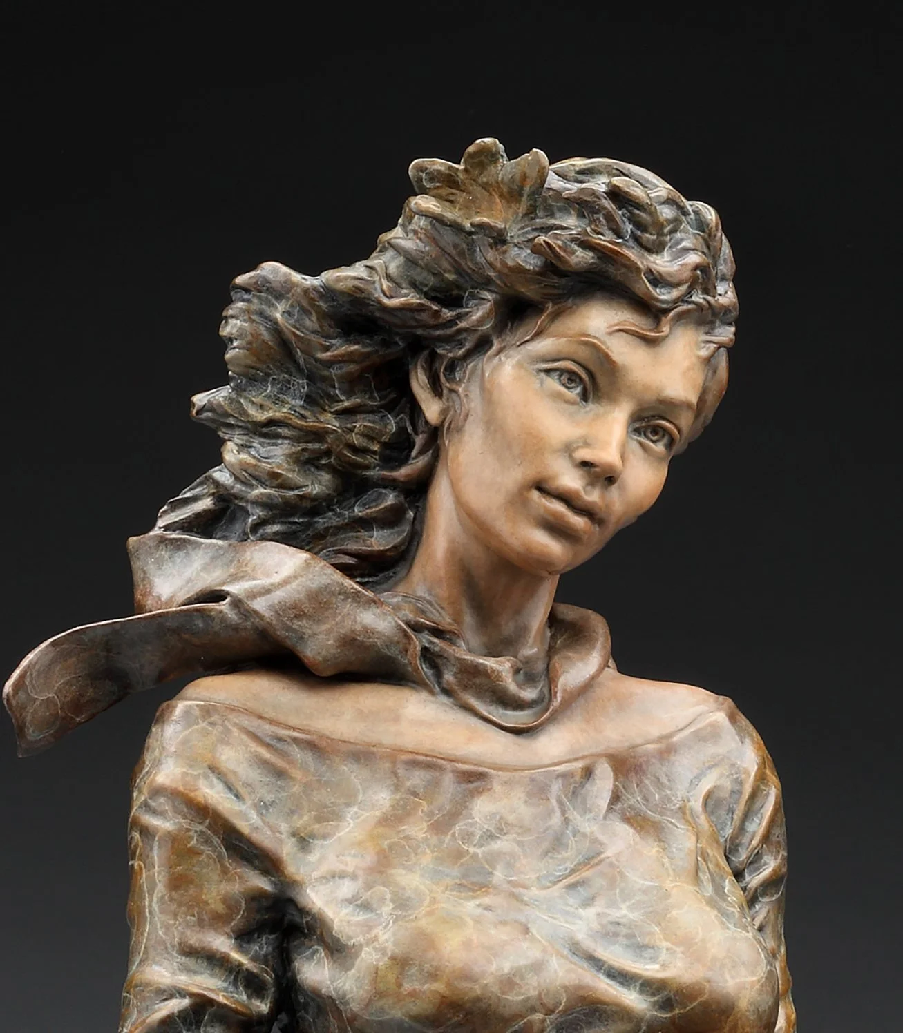 A sculpture of a woman's bust with flowing hair, wearing a scarf and a textured top, against a dark background.