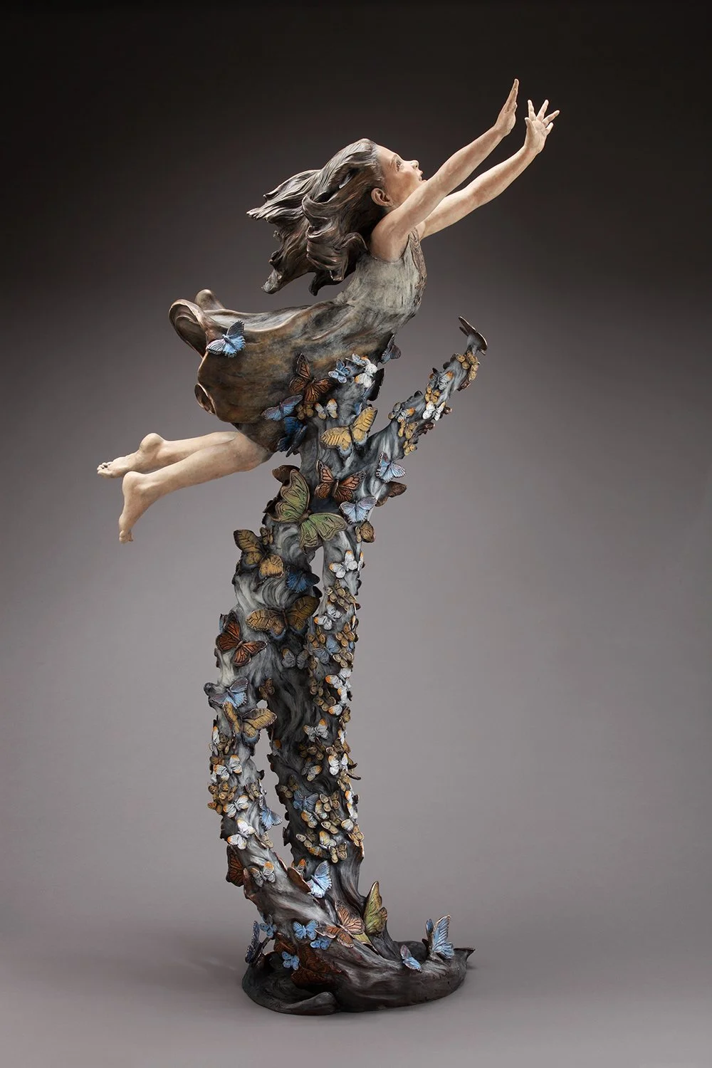 A sculpture of a young girl with flowing hair flying upward, surrounded by butterflies, and positioned on a curved, butterfly-covered base.