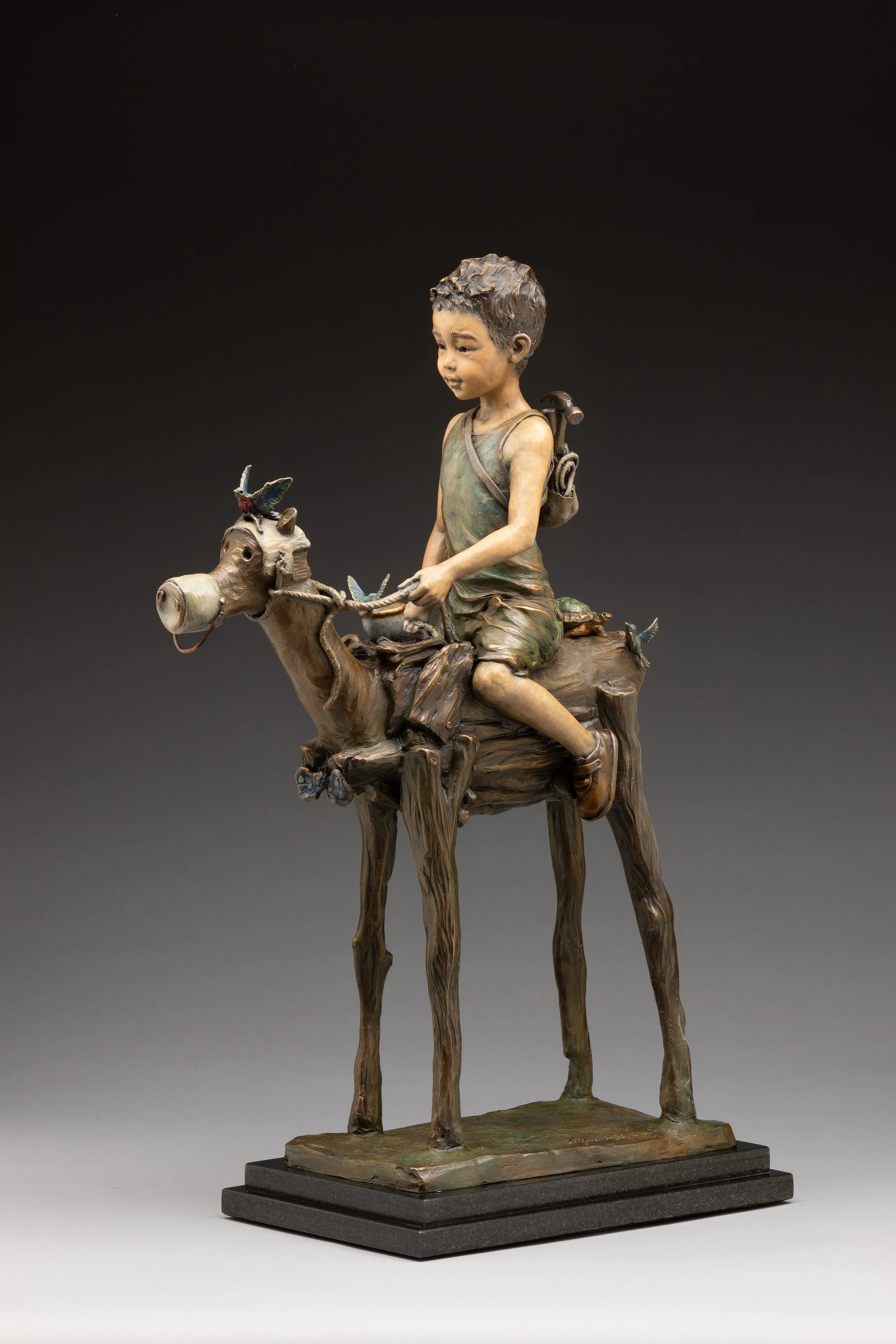 Statue of a young boy riding a camel, with a backpack, set against a dark background.