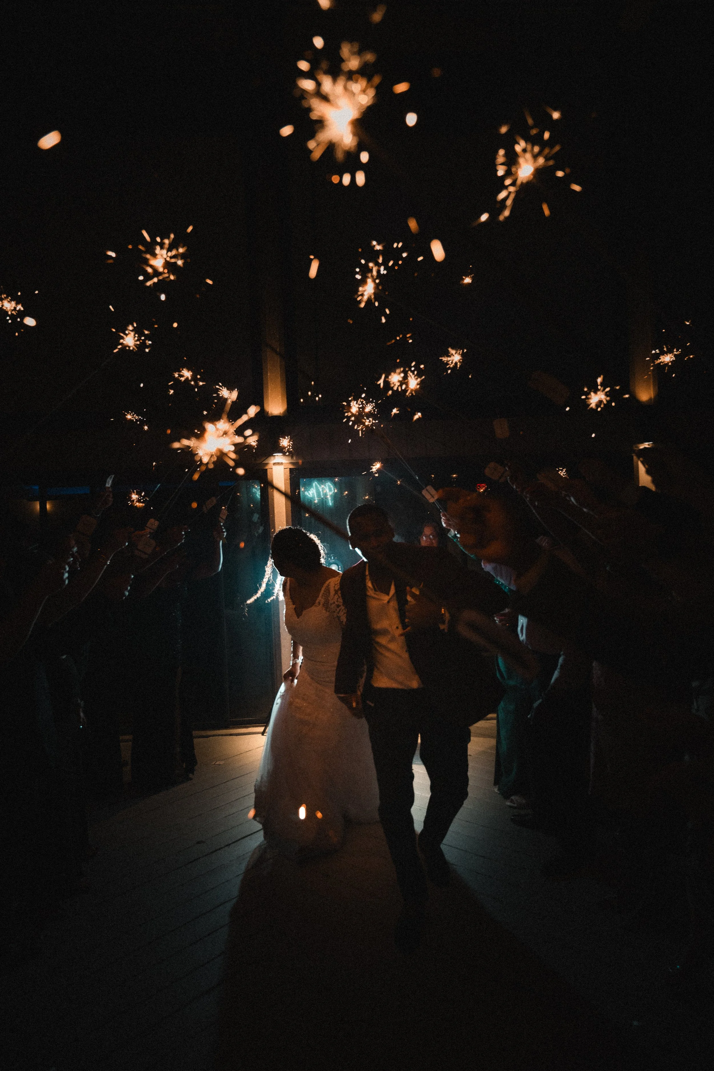 Couple dancing at a celebration under sparklers in a dimly lit indoor venue.