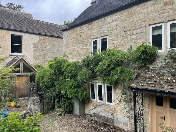 Stone house with greenery growing along the wall and a bench in the yard.
