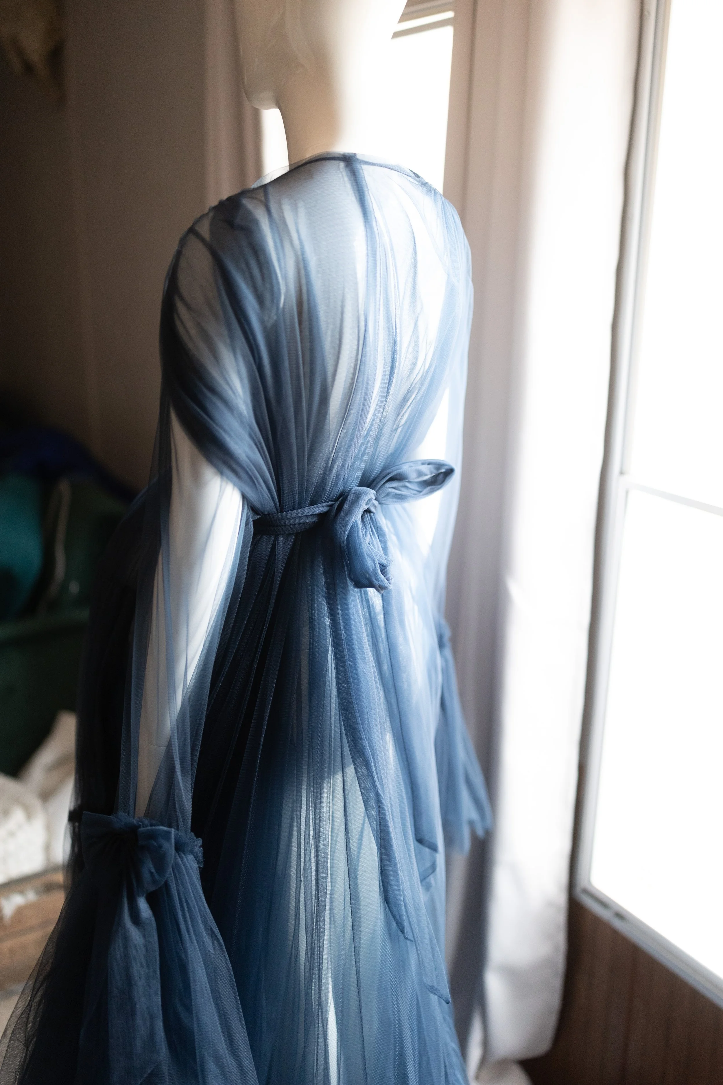 Back view of navy blue sheer wrap maternity gown with delicate tie at the waist and translucent layered fabric draping softly.