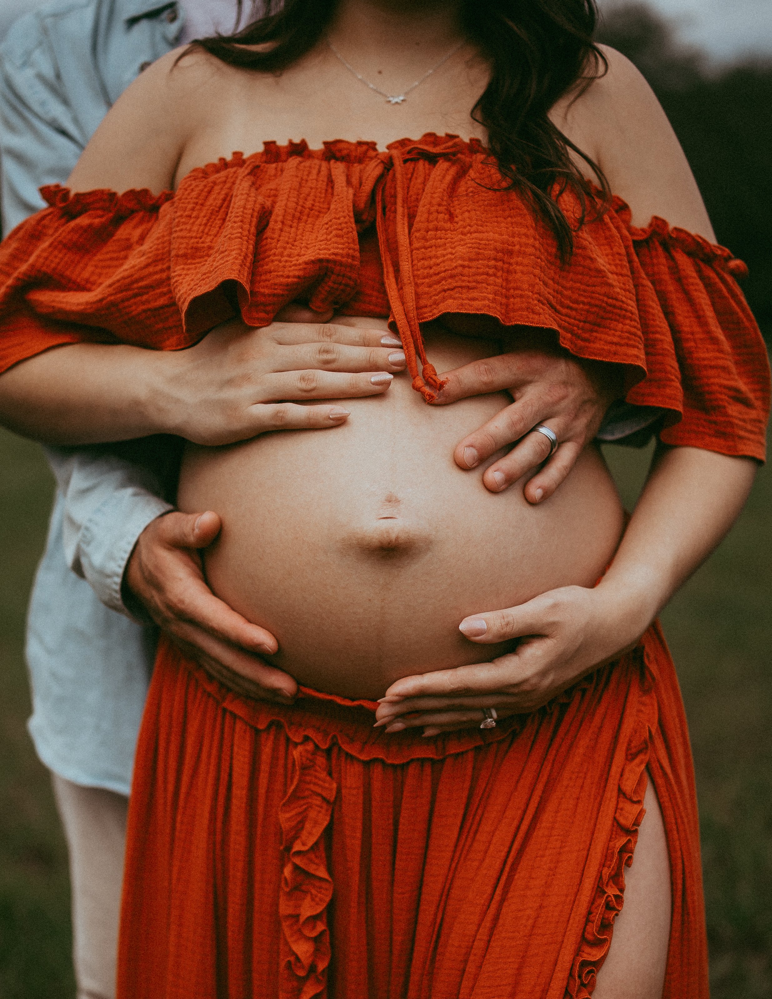 Expectant parents cradle their baby bump in a close-up maternity portrait during an outdoor session in Hilliard, Florida.