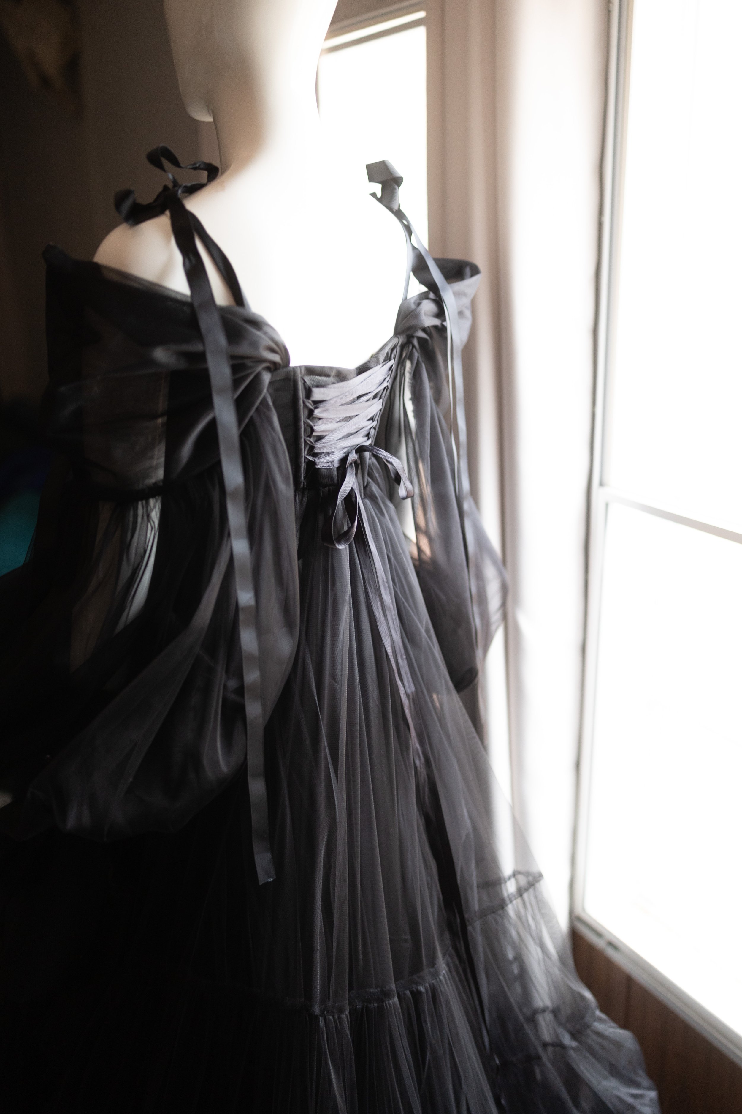 Back view of elegant black maternity dress with lace-up corset detail, soft tulle layers, and ribbon shoulder ties.