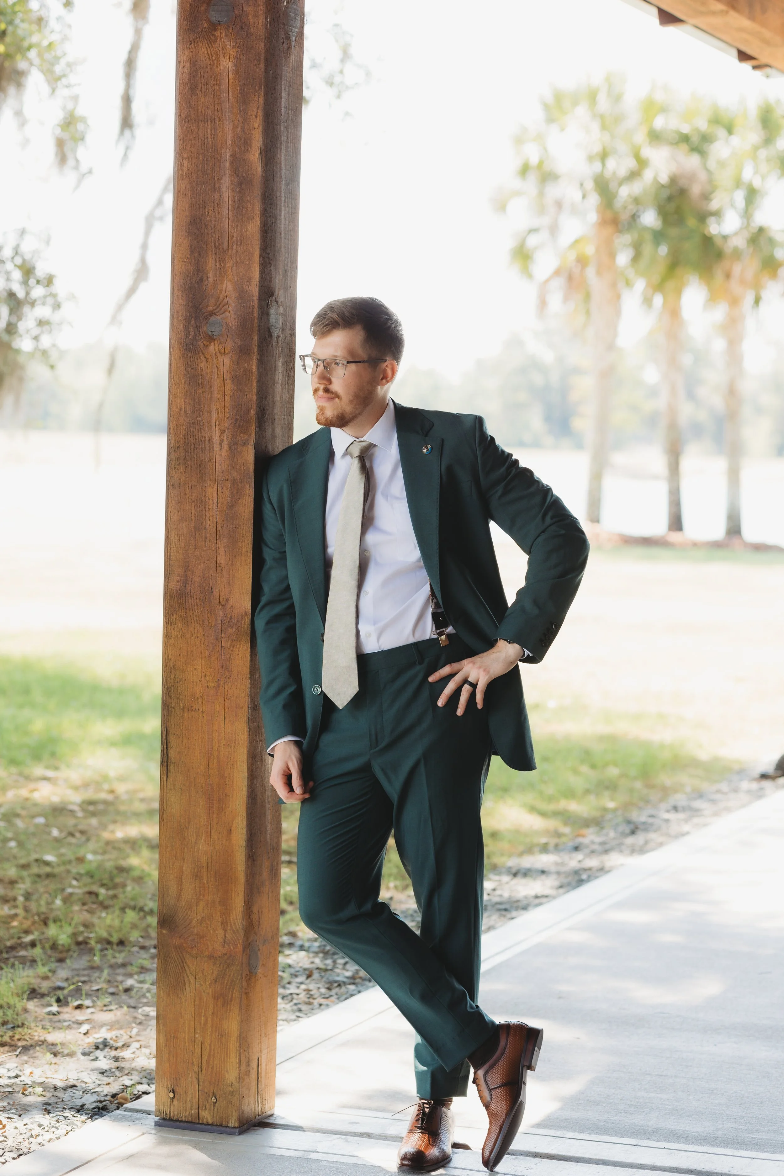 The groom leans against a wooden post for a relaxed portrait before the ceremony.