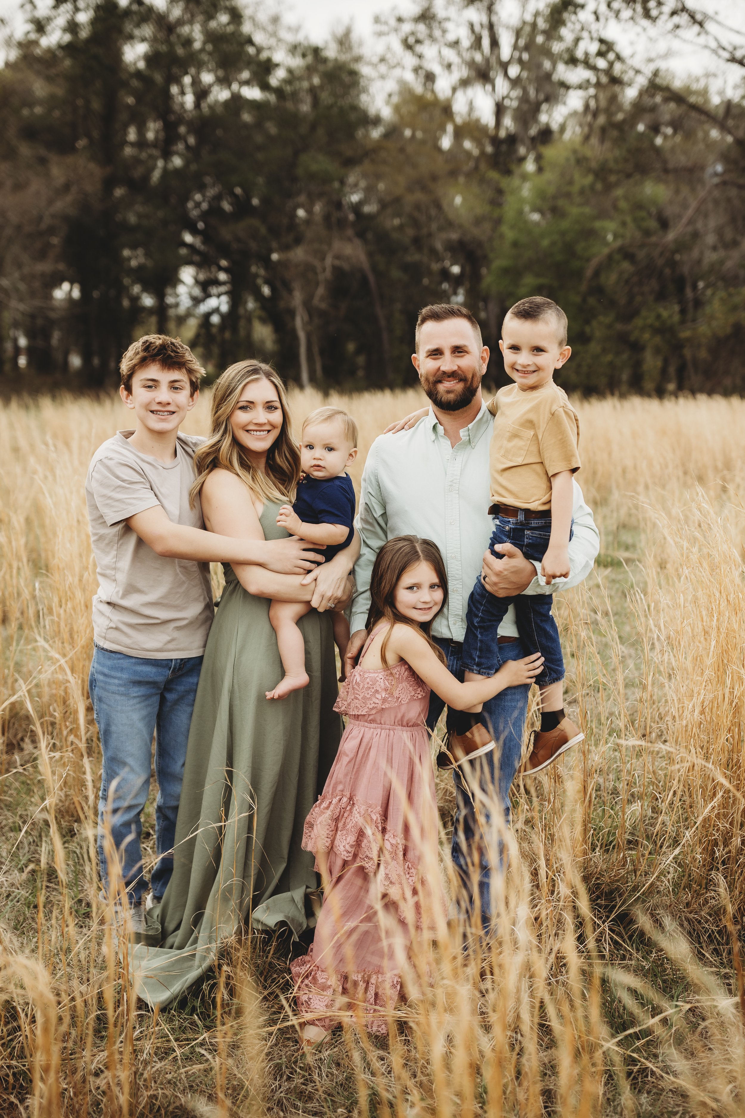 Family of six smiling together in a tall grass field during an outdoor family photography session in Northeast Florida.