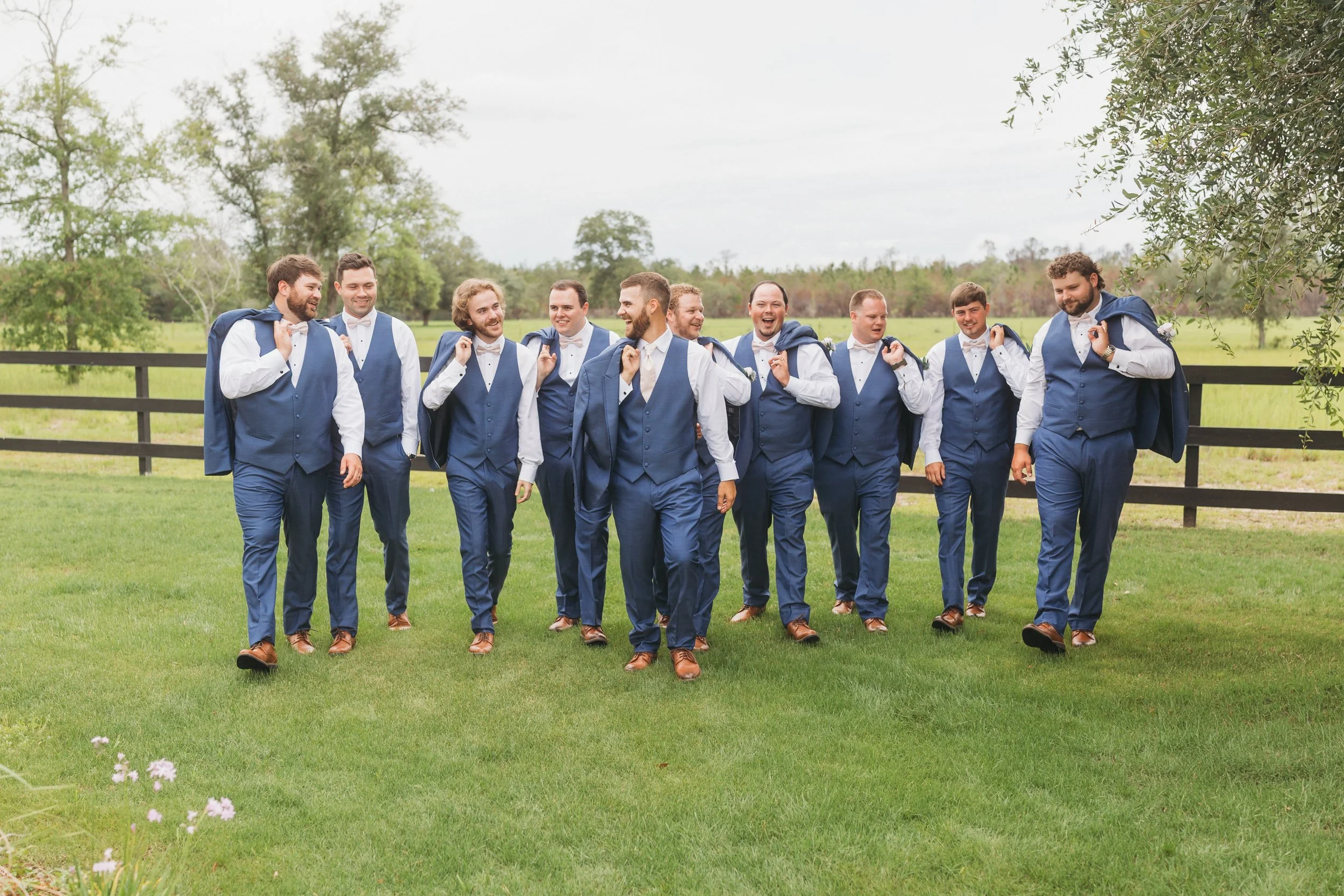 Dylan and his groomsmen laugh while walking across the lawn in matching blue suits at Red River Estate in Waynesville, Georgia.