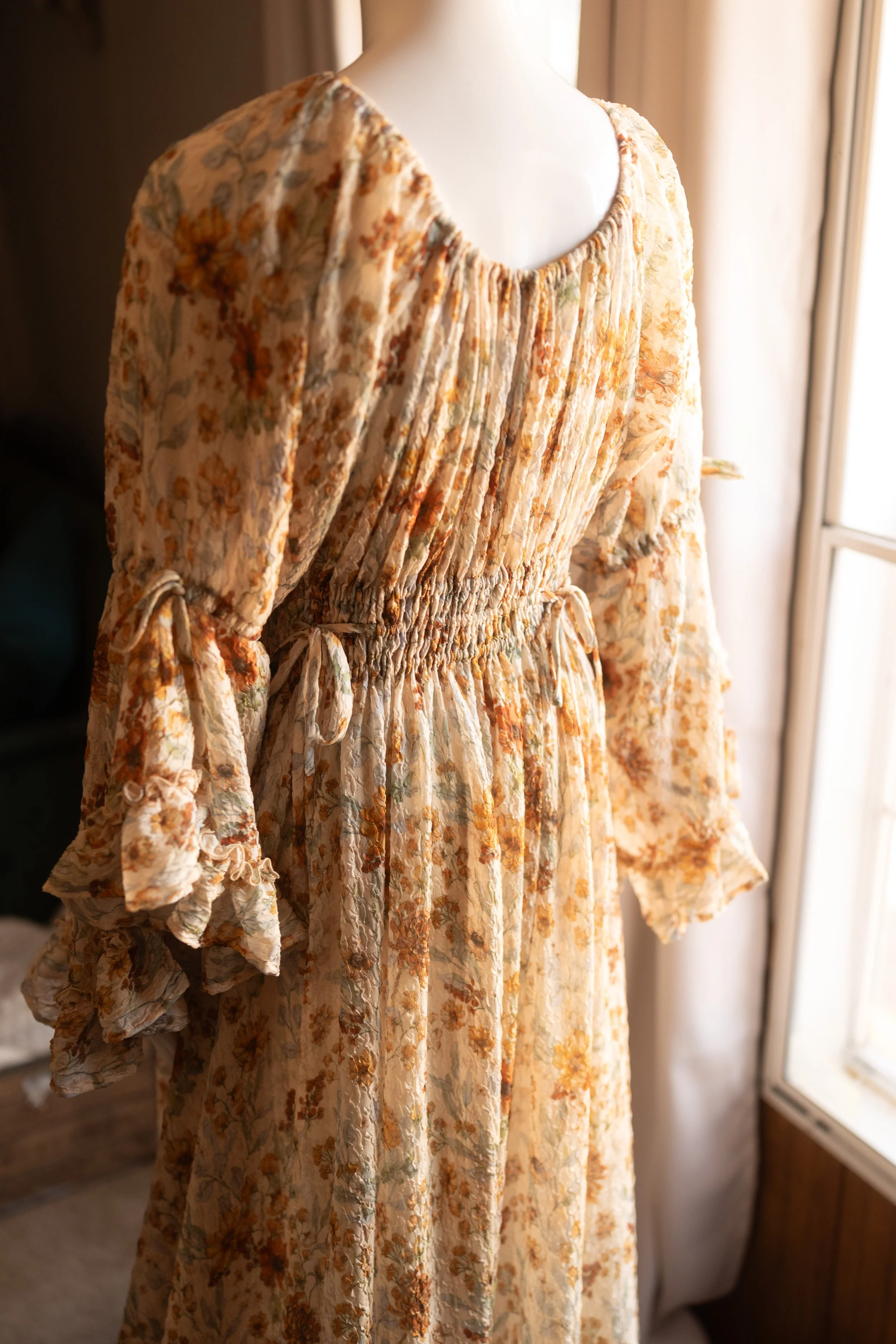 Close-up of a light, airy floral maternity gown with warm tones, soft gathers, and a flowing silhouette.