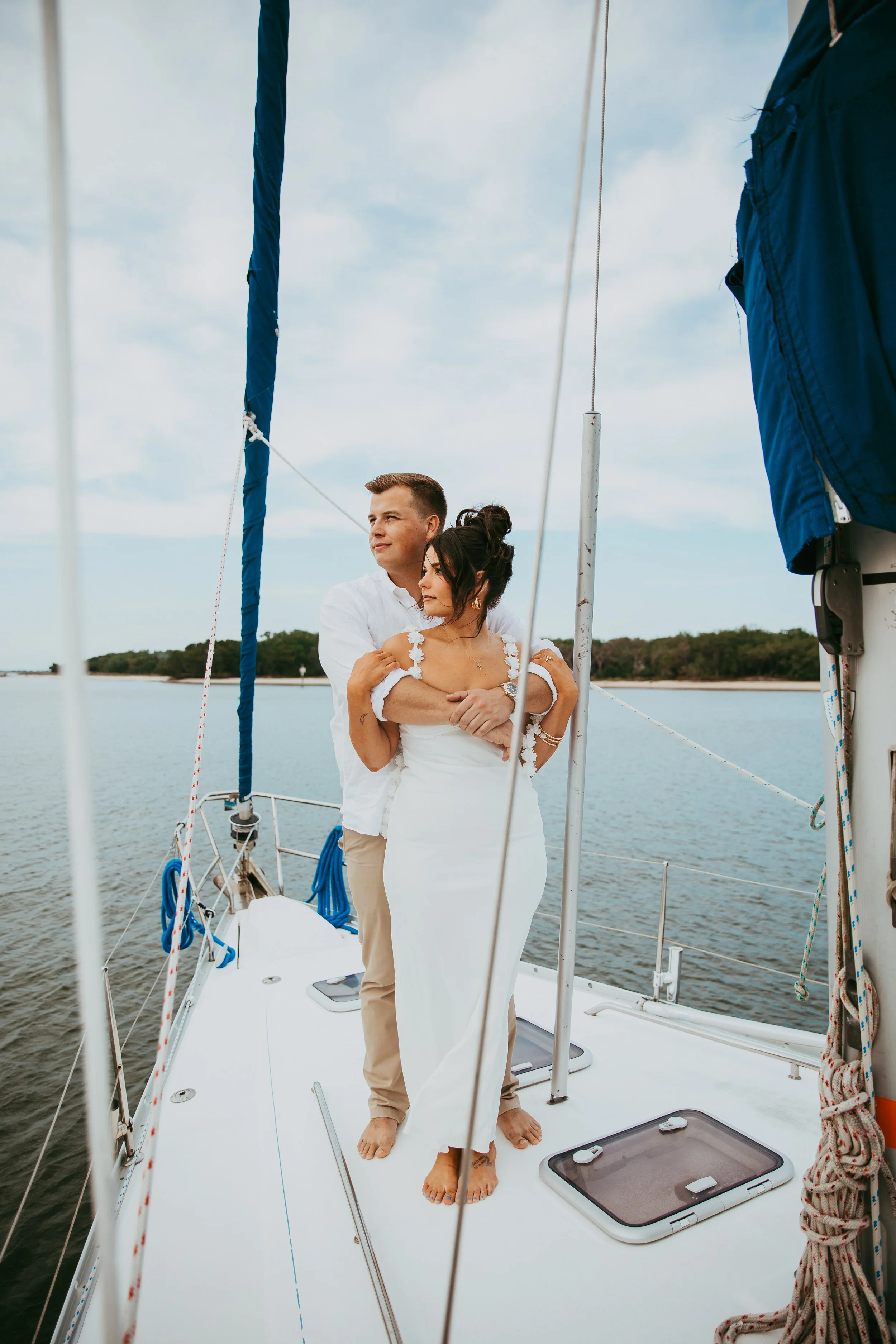 Engaged couple stands barefoot together on the bow of a sailboat near Fernandina Beach