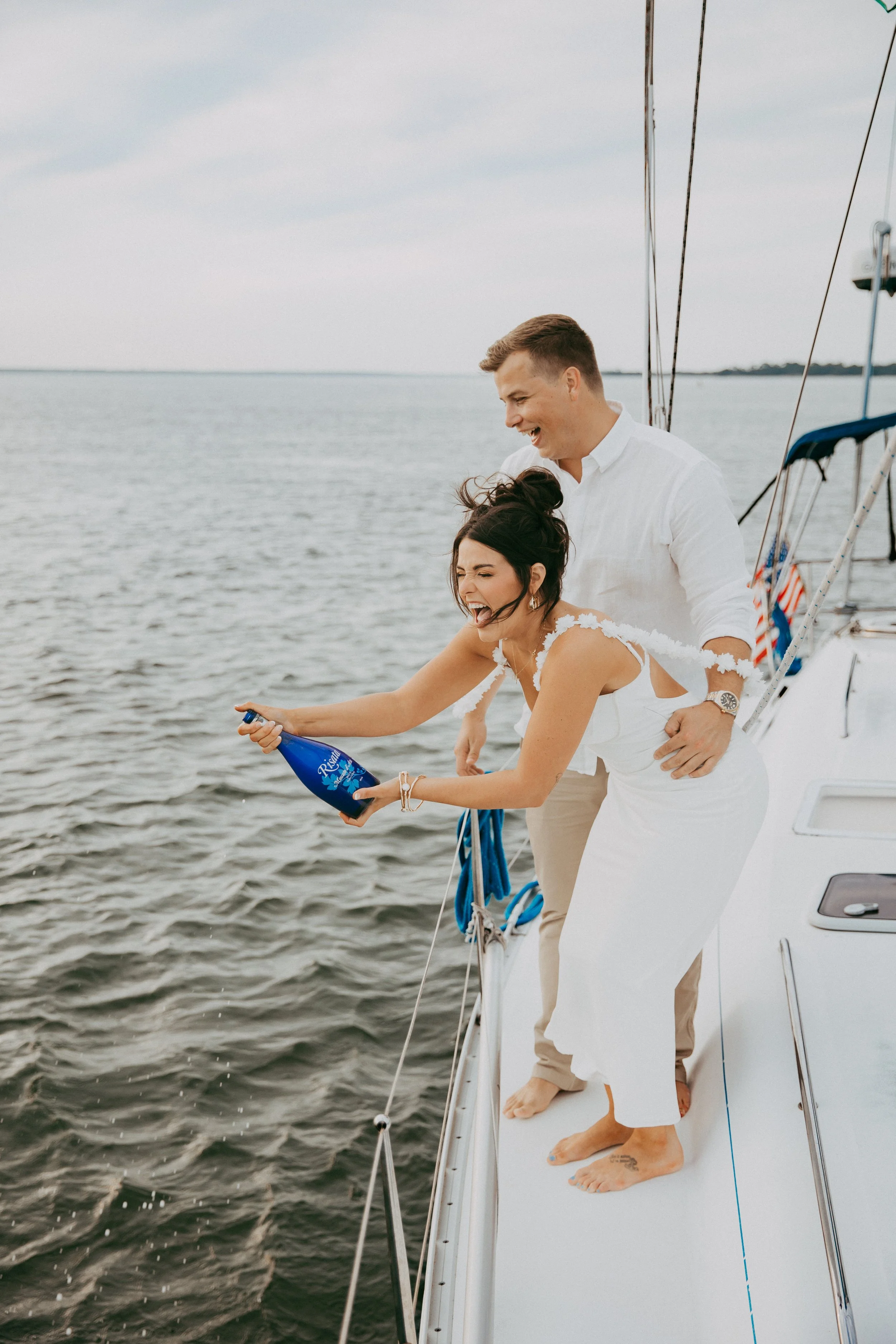 Lyndsey and Adam laugh together with a bottle on the sailboat deck.