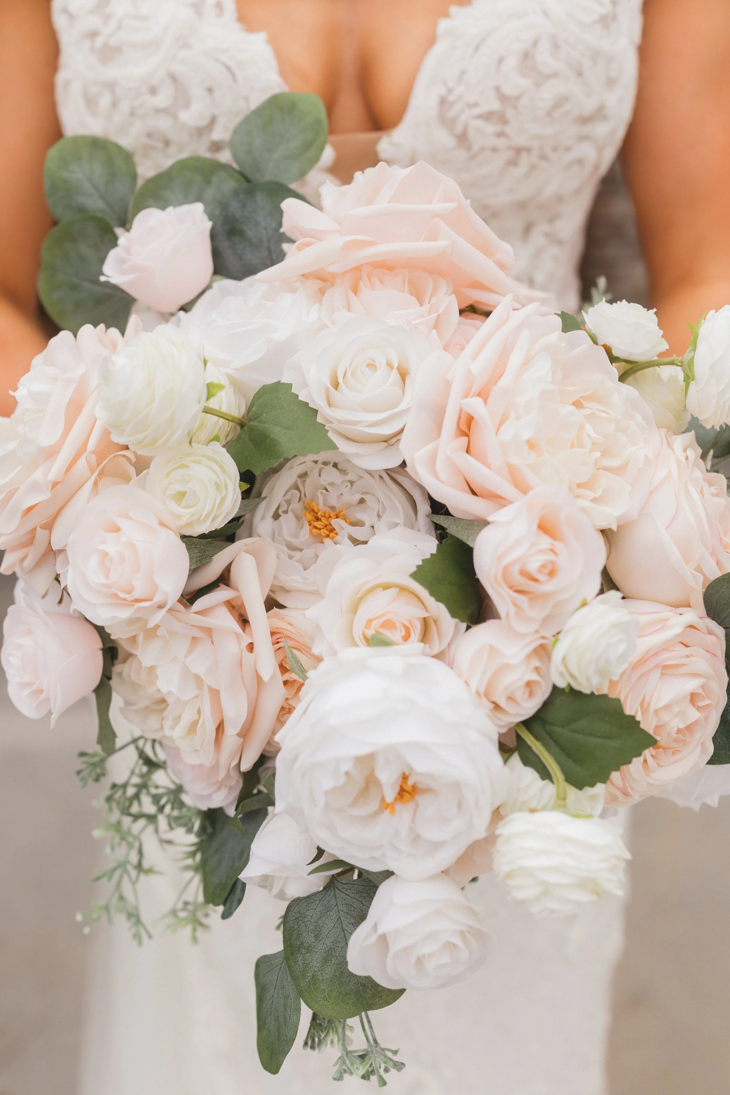 Close-up of Emma holding a romantic bridal bouquet of blush and ivory roses with eucalyptus greenery.
