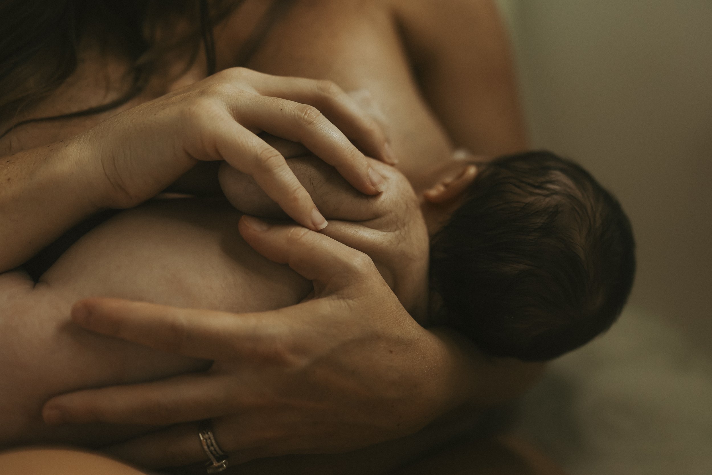 Close-up of a parent holding and nursing a newborn, with hands gently supporting the baby’s head and body.