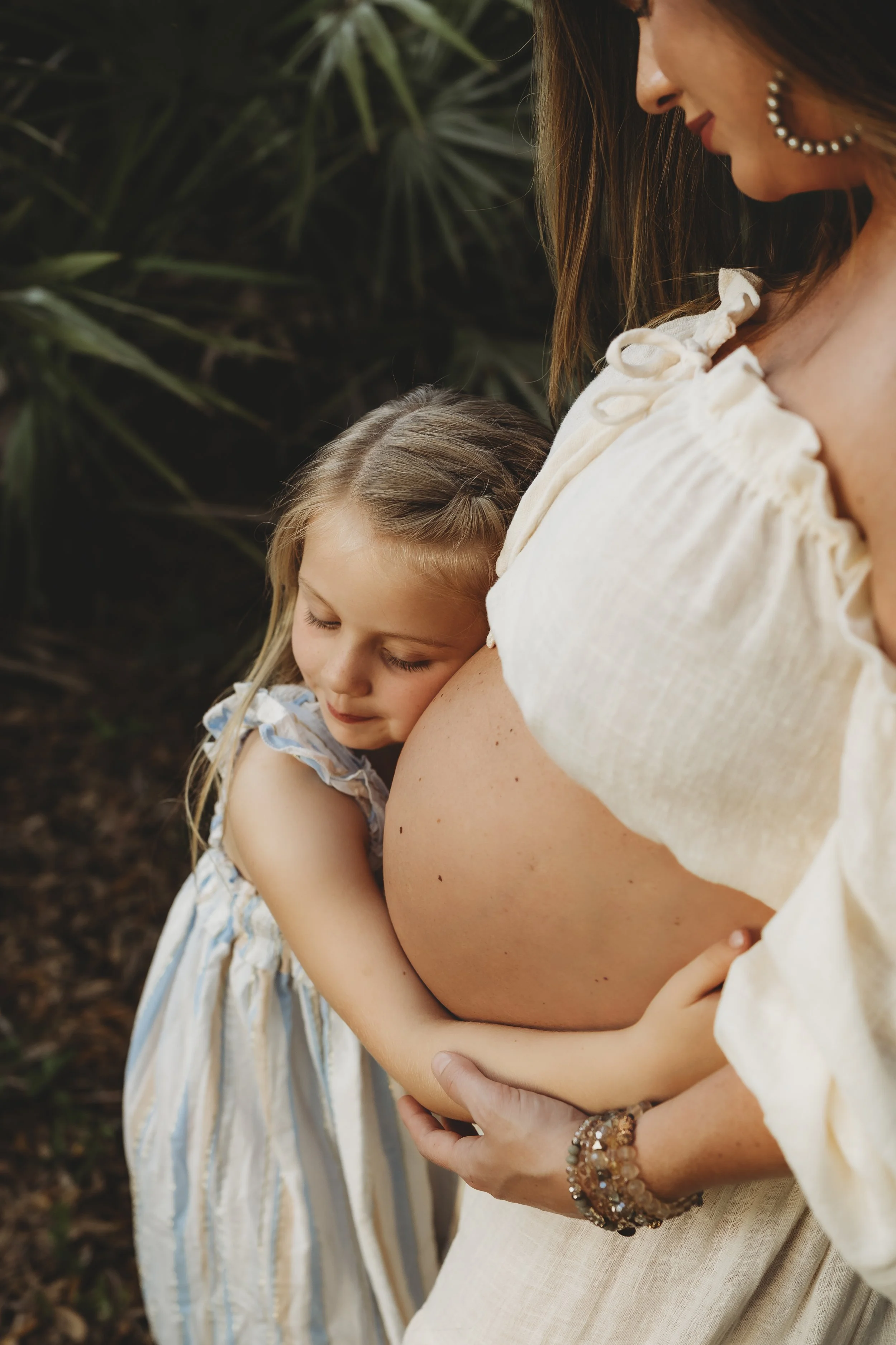 Tender maternity photo of an expectant mother and her daughter sharing a peaceful moment as the child embraces her baby bump.