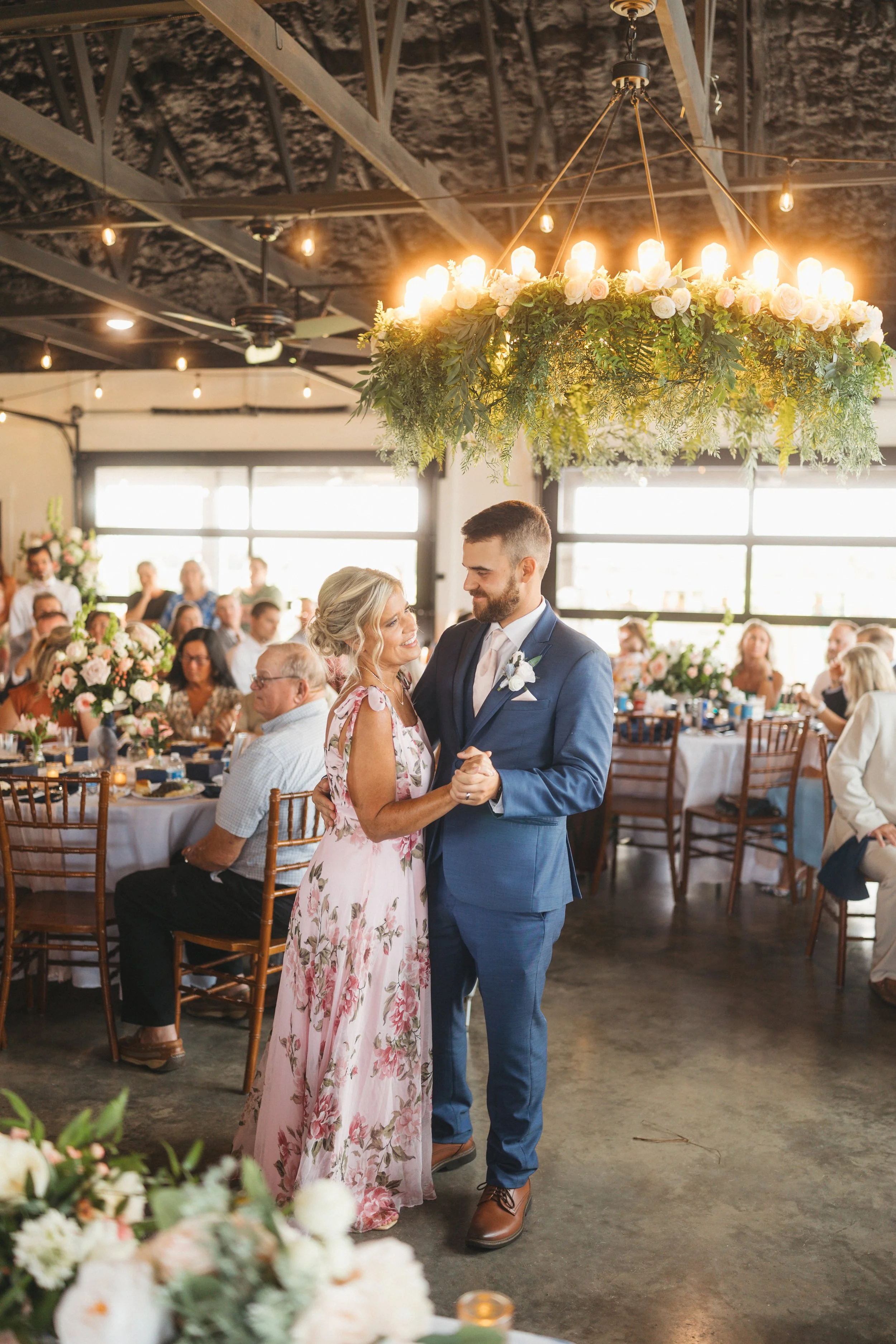 Dylan shares a mother-son dance with his mom beneath a floral chandelier during the reception at Red River Estate.