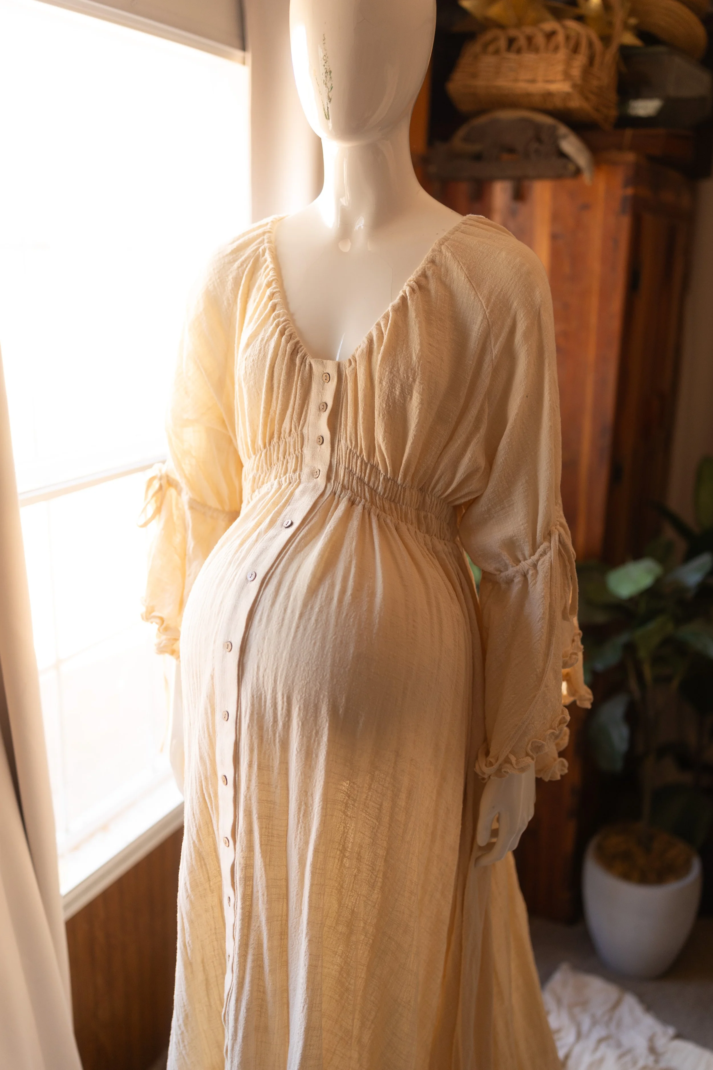 Romantic cream maternity dress with flowing sleeves and a button-front design, softly glowing in natural window light.