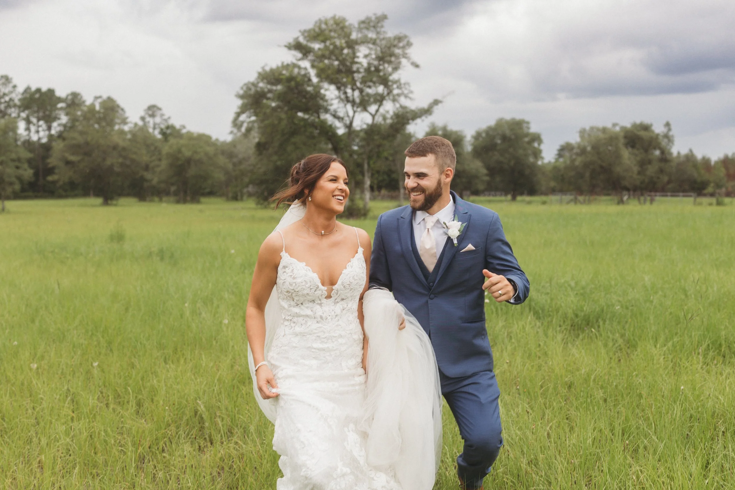 Bride and groom laughing together while walking through a green field on their wedding day in Northeast Florida.