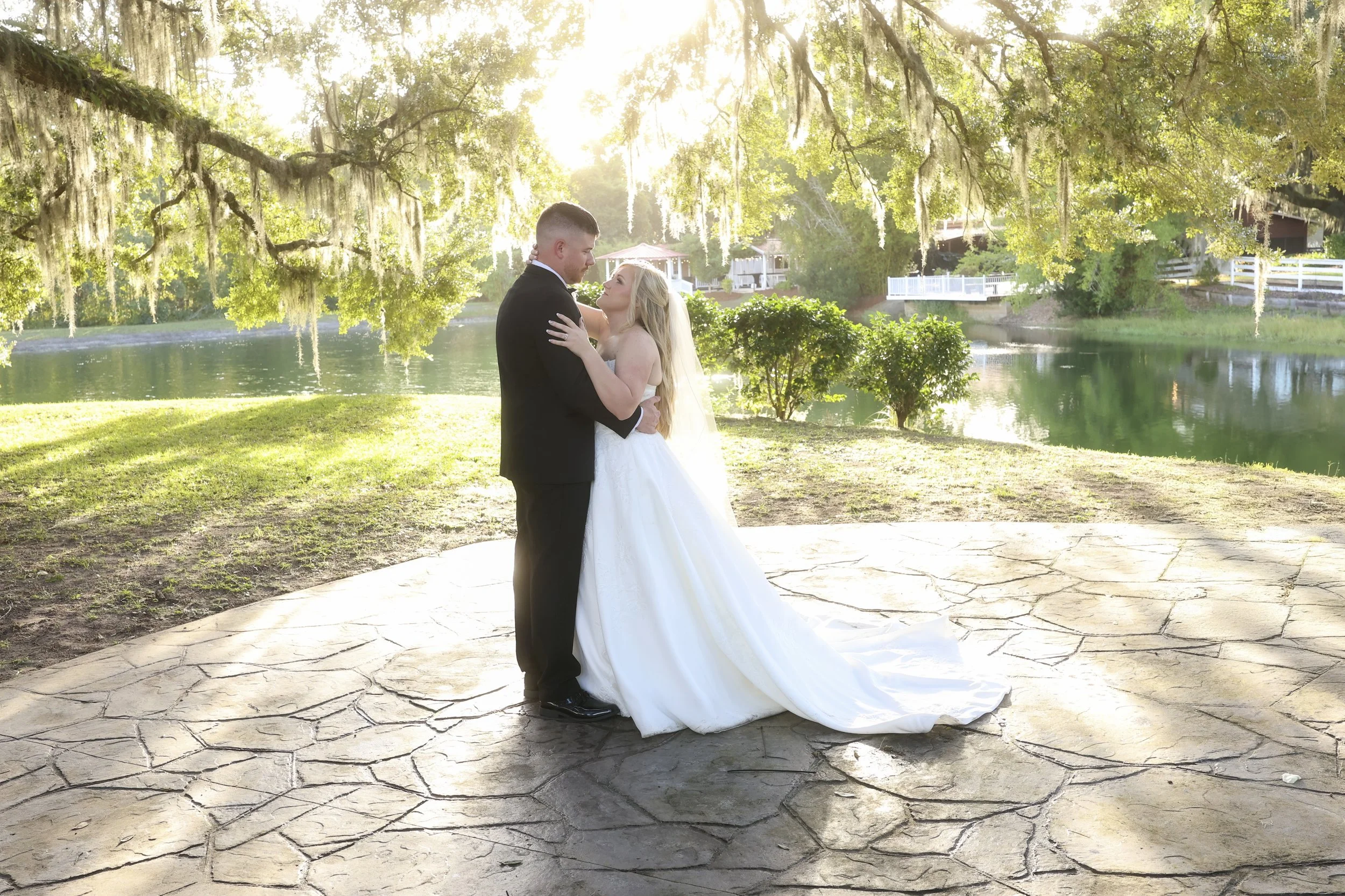 Wrapped in golden light, the bride and groom hold each other beneath moss-draped oak trees by the water at Layton’s Land-n, sharing a quiet, timeless moment as the day fades into forever.