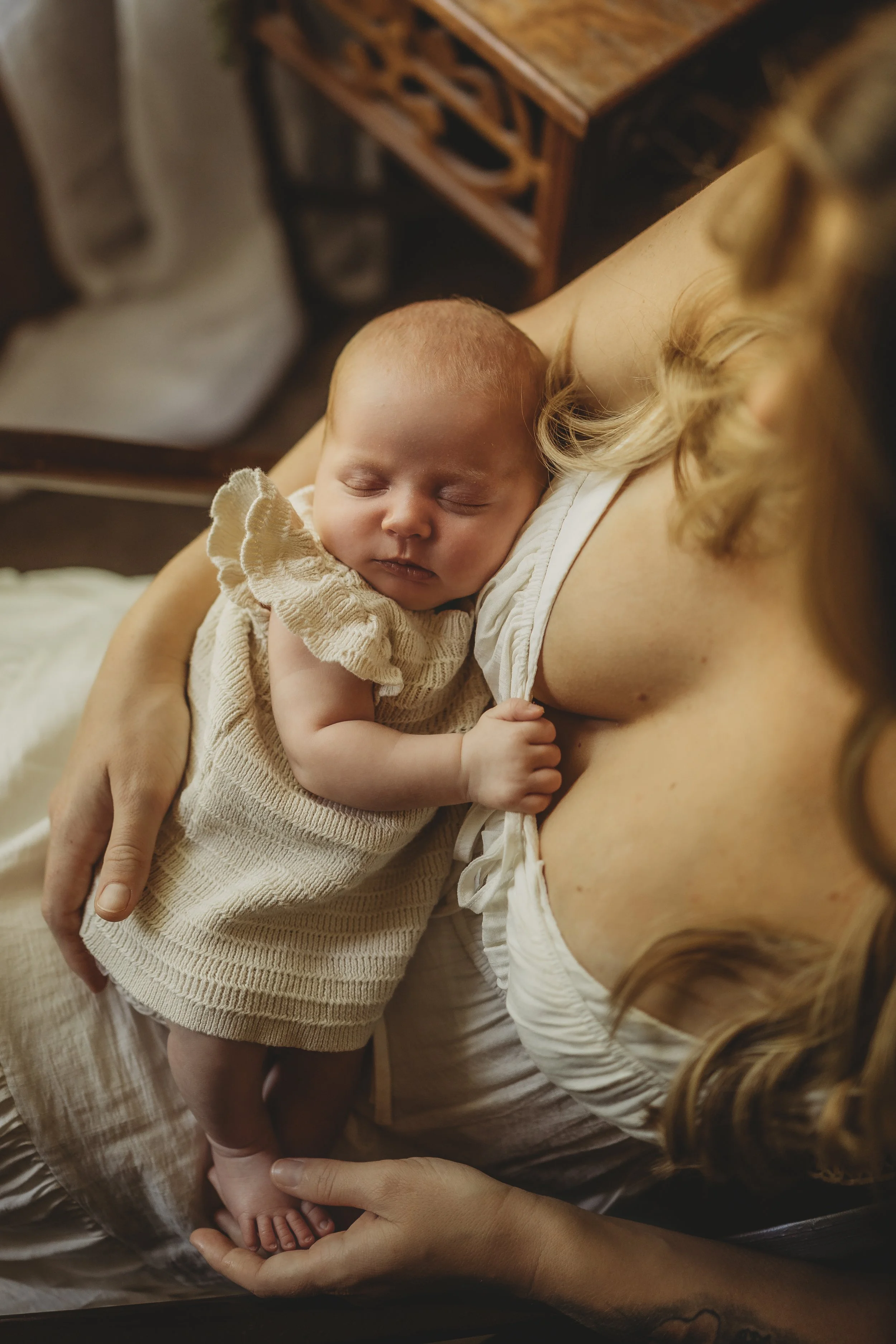 Sleeping newborn nestled against their mother’s chest, tiny hand resting gently as they share a quiet, peaceful moment indoors.
