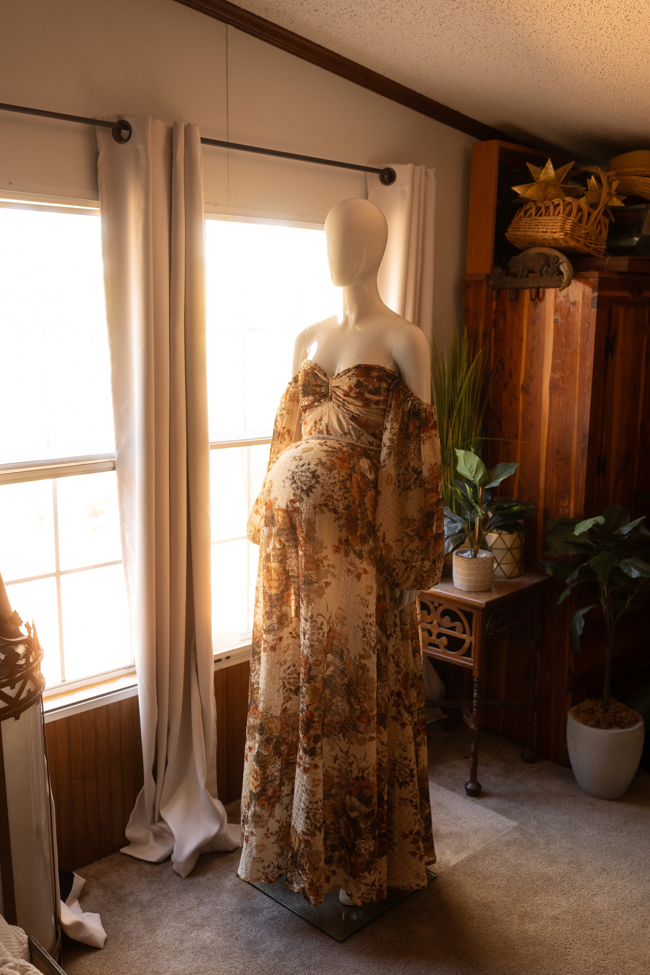 Earthy boho maternity dress with floral texture, off-the-shoulder sleeves, and a flowing skirt, displayed on a mannequin in natural light.