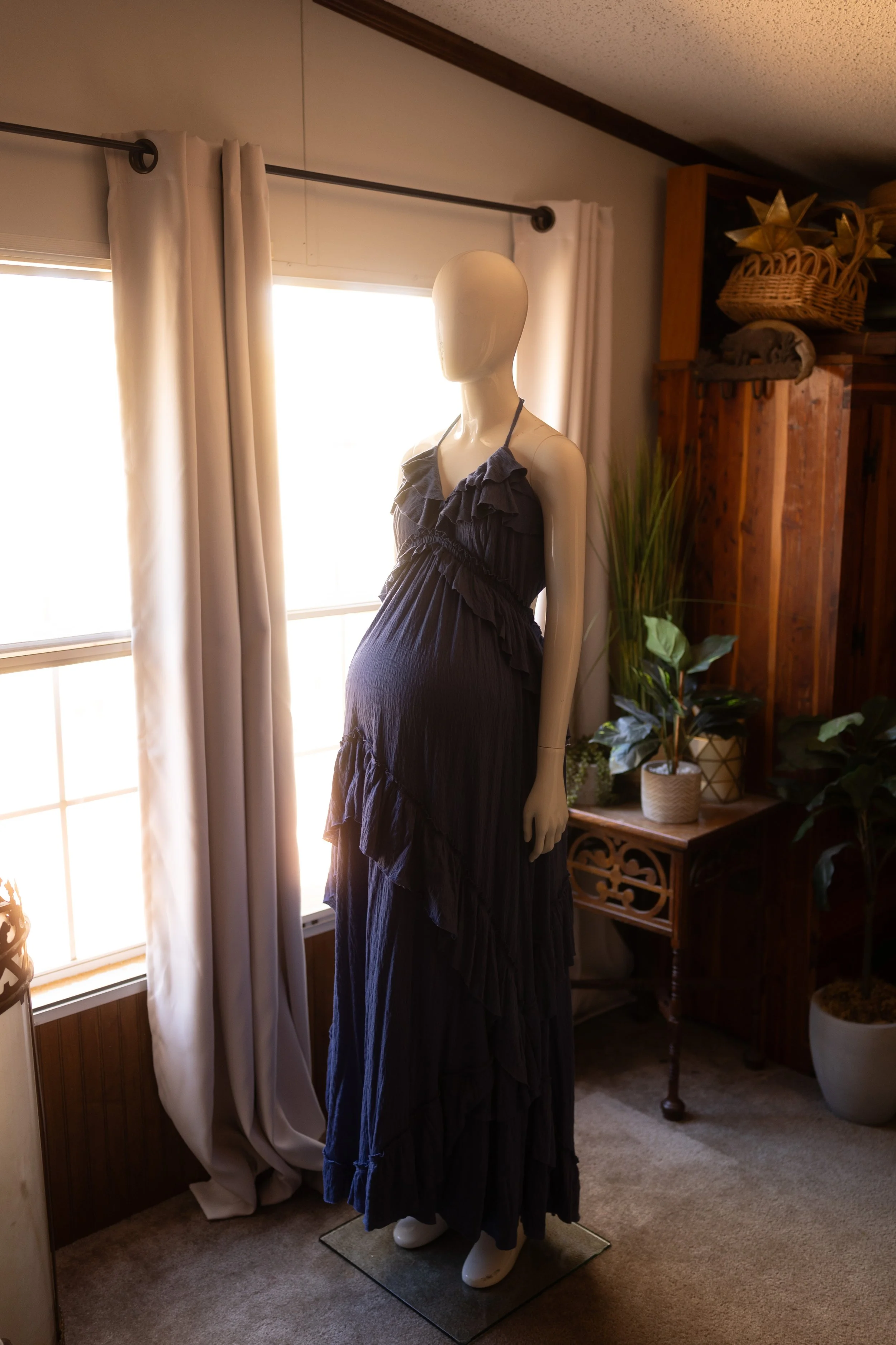 Feminine maternity dress in a deep muted tone with layered ruffles and an open back, displayed on a mannequin in natural light.