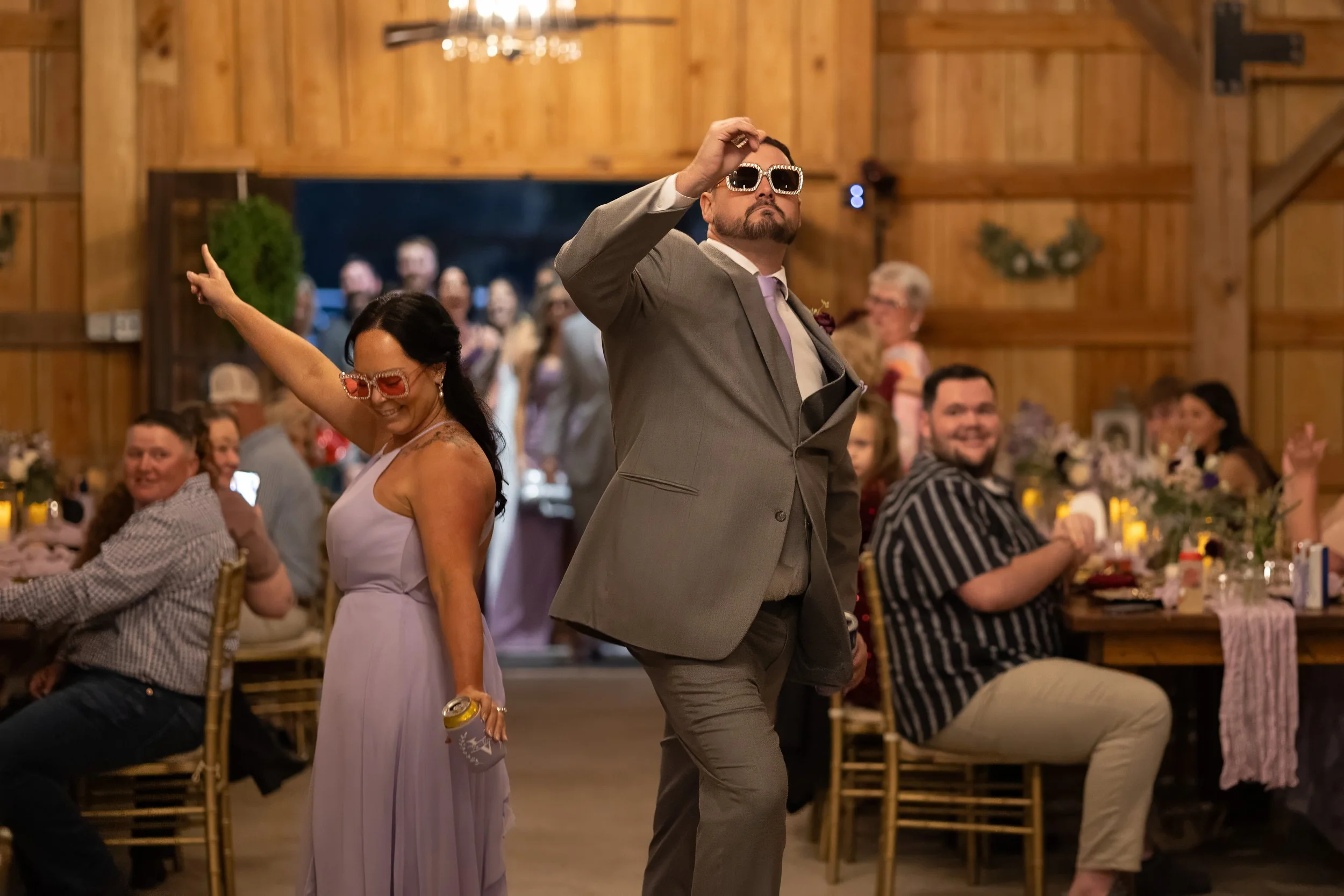 Reception entrance moment as a wedding party member dances down the aisle wearing sunglasses.