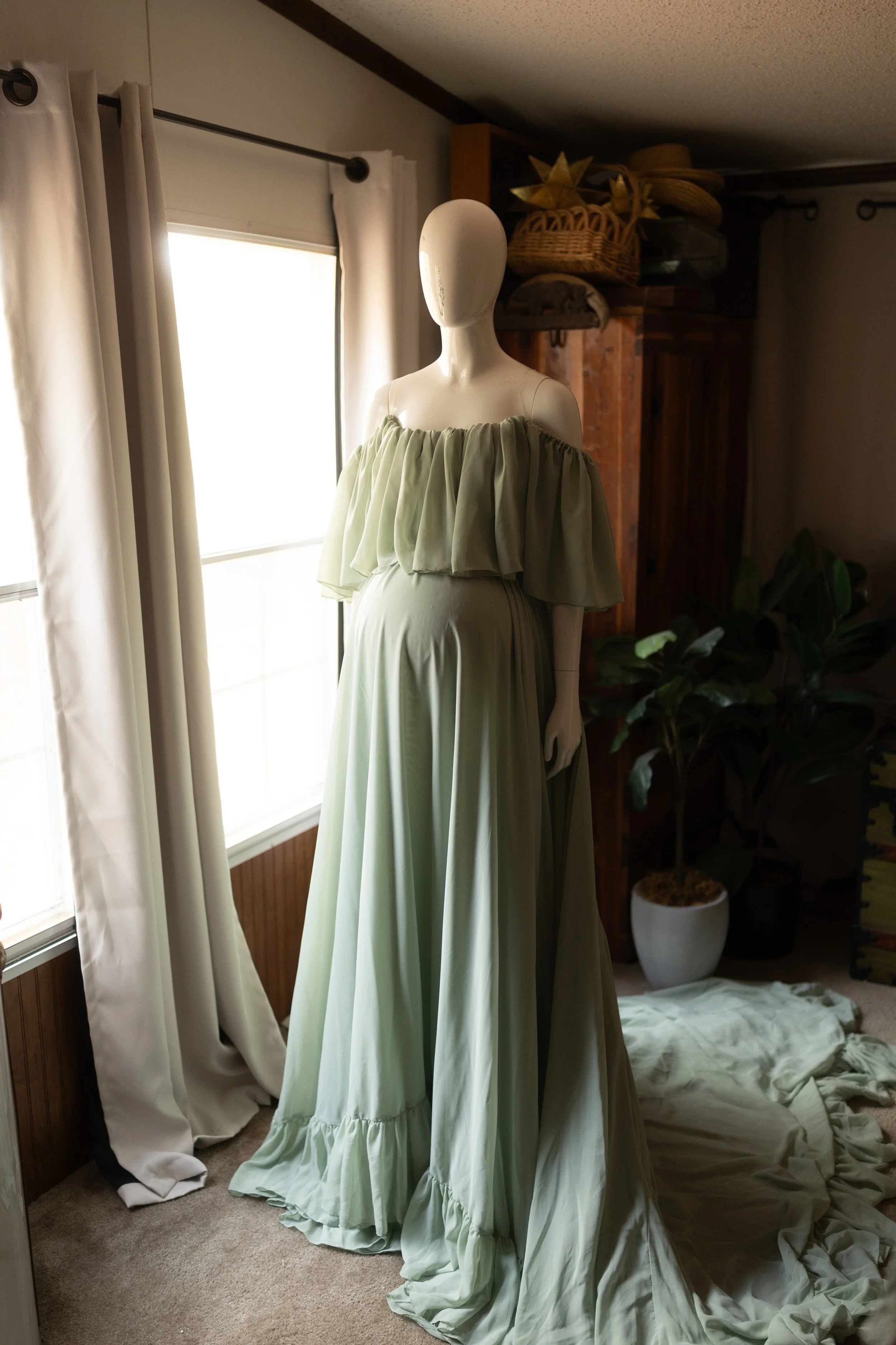 Flowy sage green chiffon maxi dress with an off-the-shoulder ruffled neckline and a soft, airy skirt, styled on a mannequin in natural light.