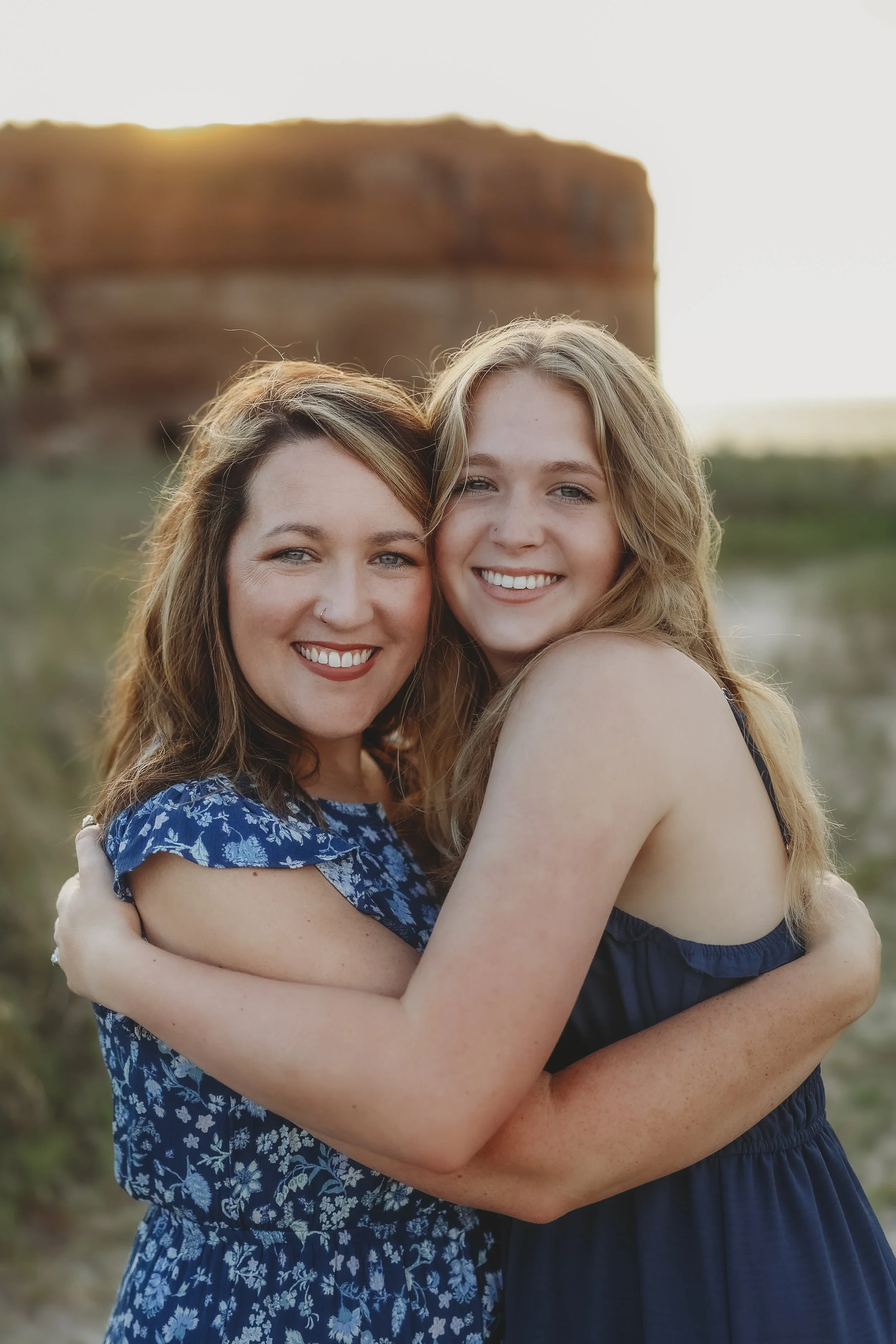 A mother and daughter embrace with warm smiles during a sunset family session by the coast.