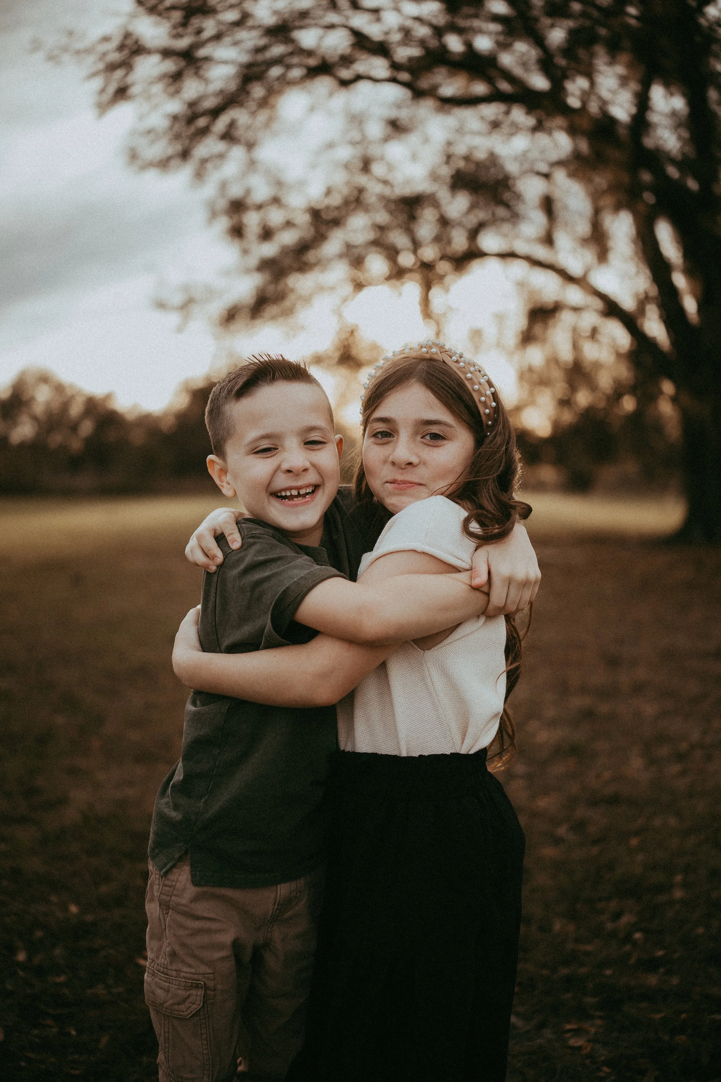 wo siblings share a warm hug and smile together during an outdoor family session.