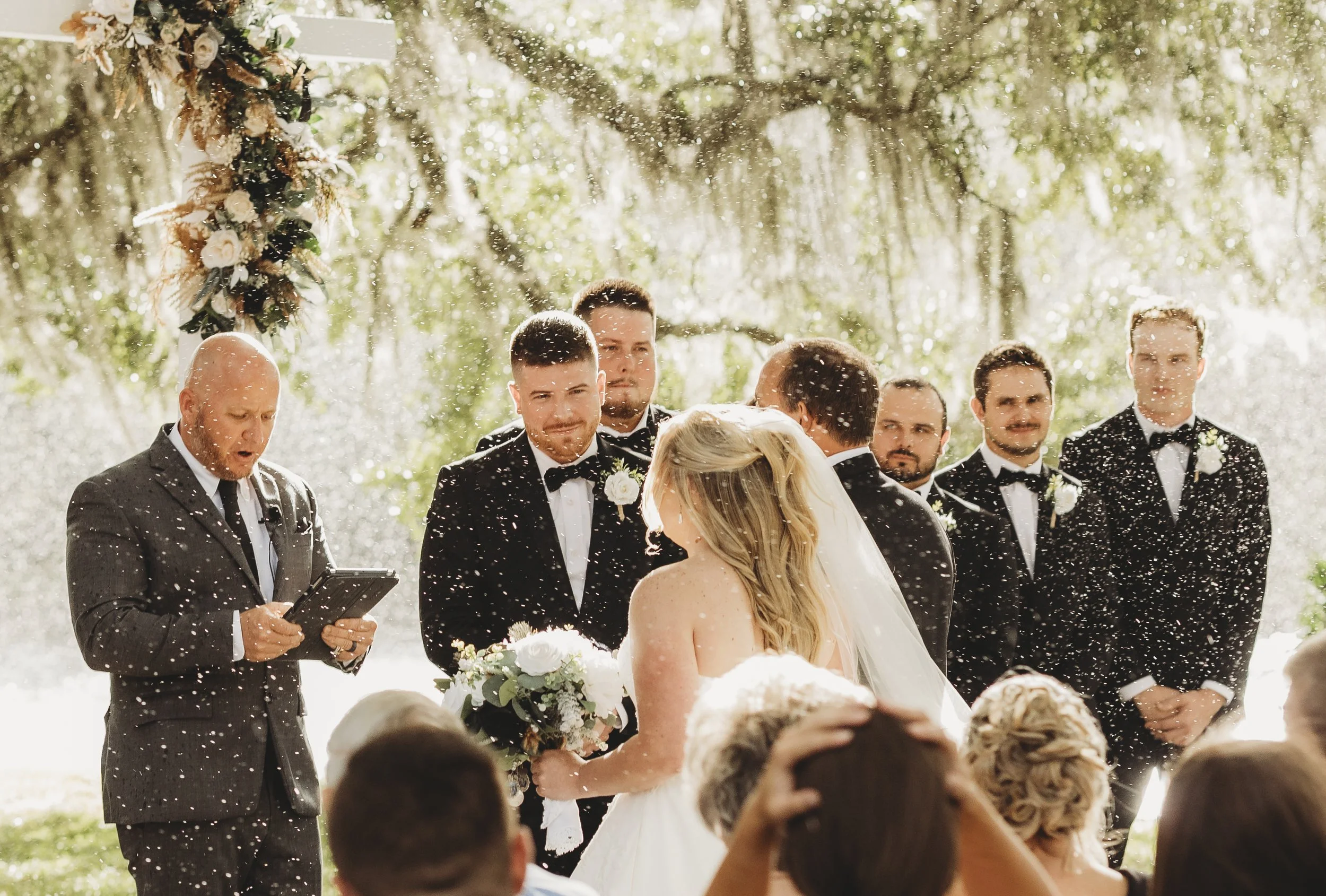 The ceremony unfolds beneath falling rain, a quiet reminder that love is steady even when the skies change.