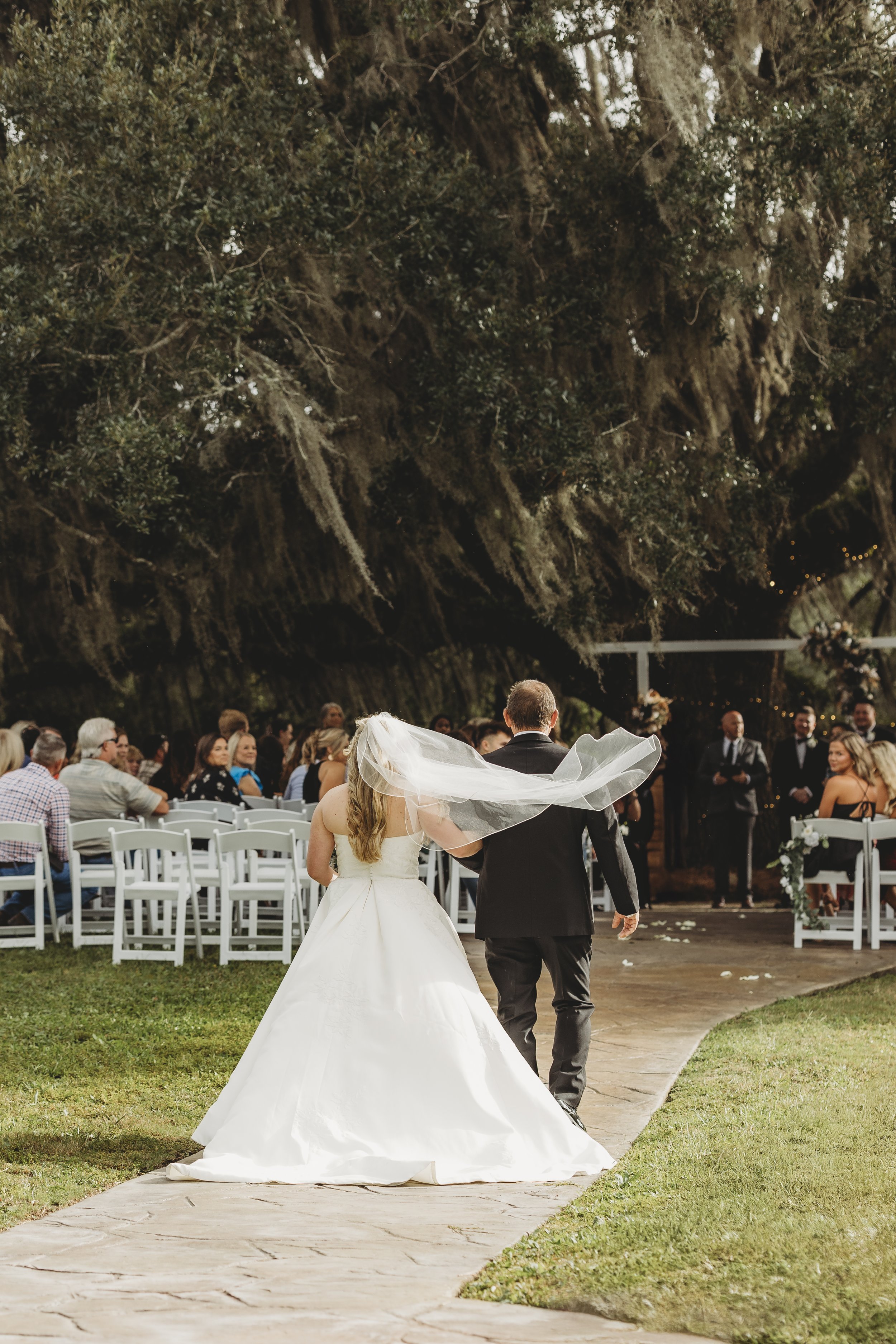 Her veil lifts as her father walks her forward, a quiet moment of love, pride, and letting go.
