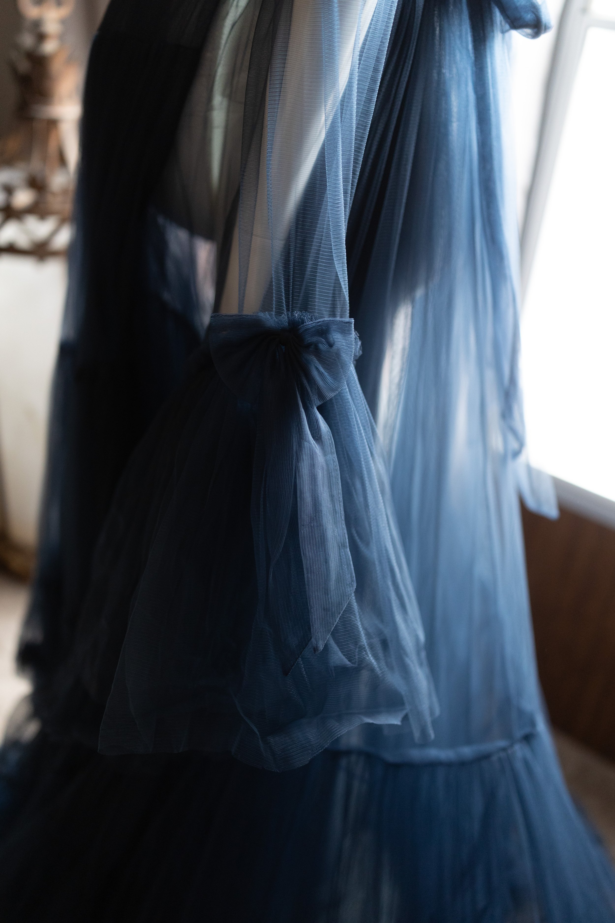 Close-up of navy blue sheer tulle maternity wrap dress sleeve featuring a soft tied bow and layered flowing fabric detail.