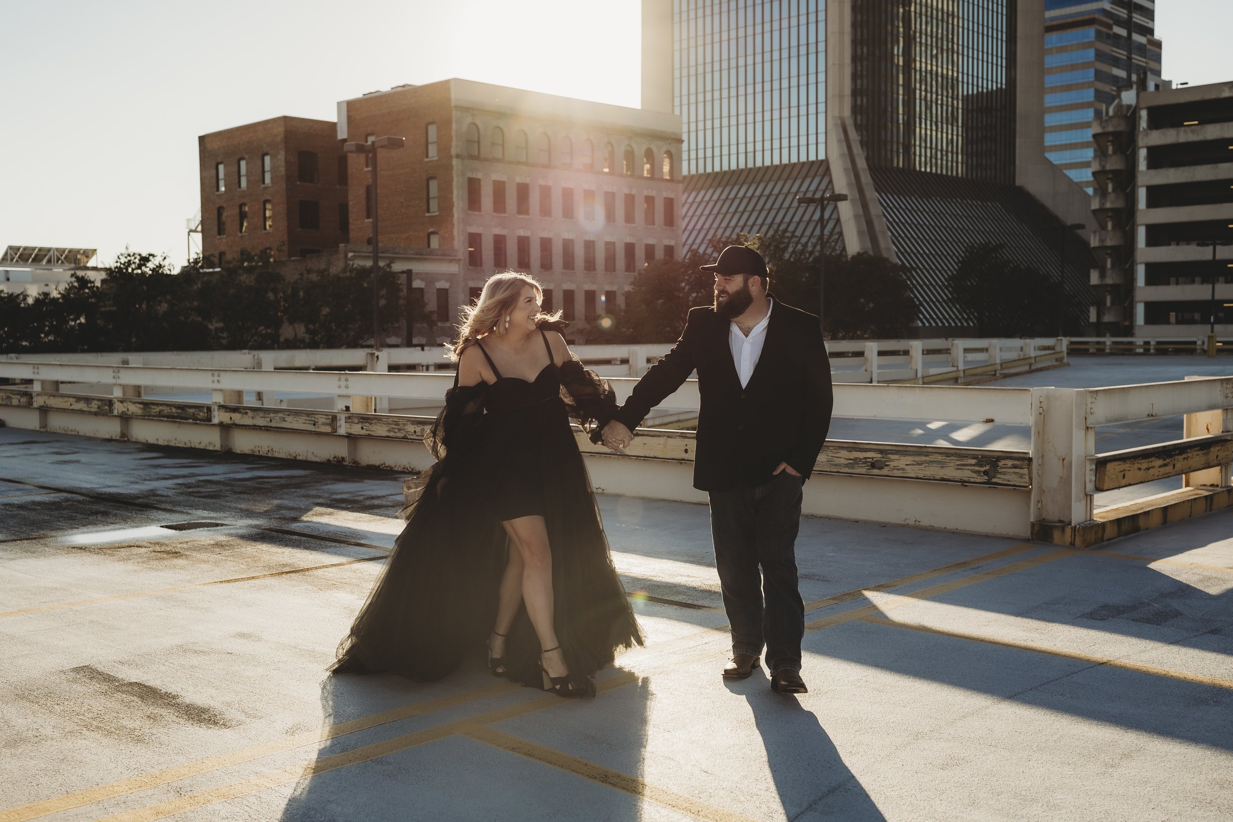 Elegant black maternity dress with flowing tulle skirt photographed on urban rooftop at sunset.