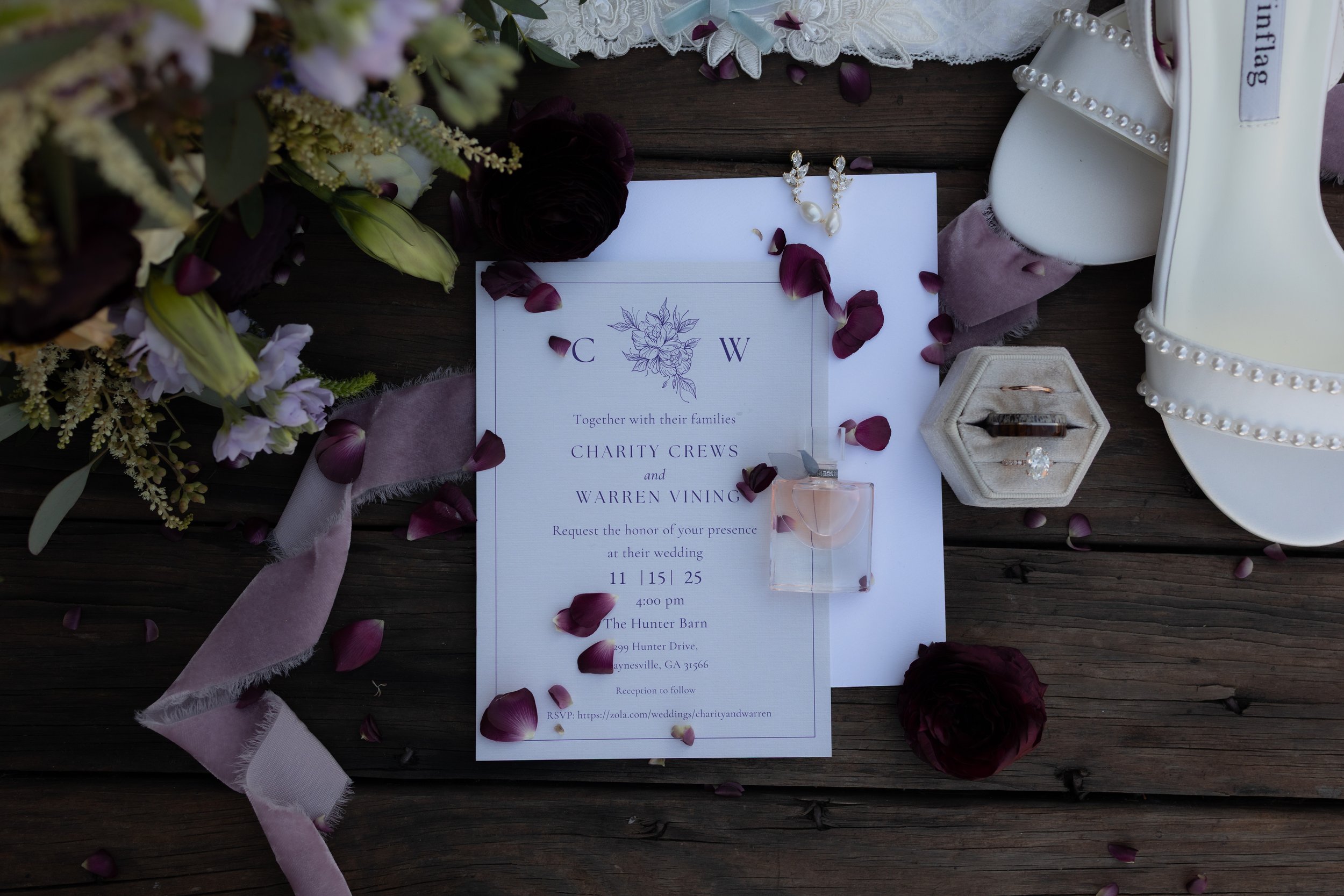 Styled wedding details featuring the invitation, rings, florals, and bridal accessories on wood.