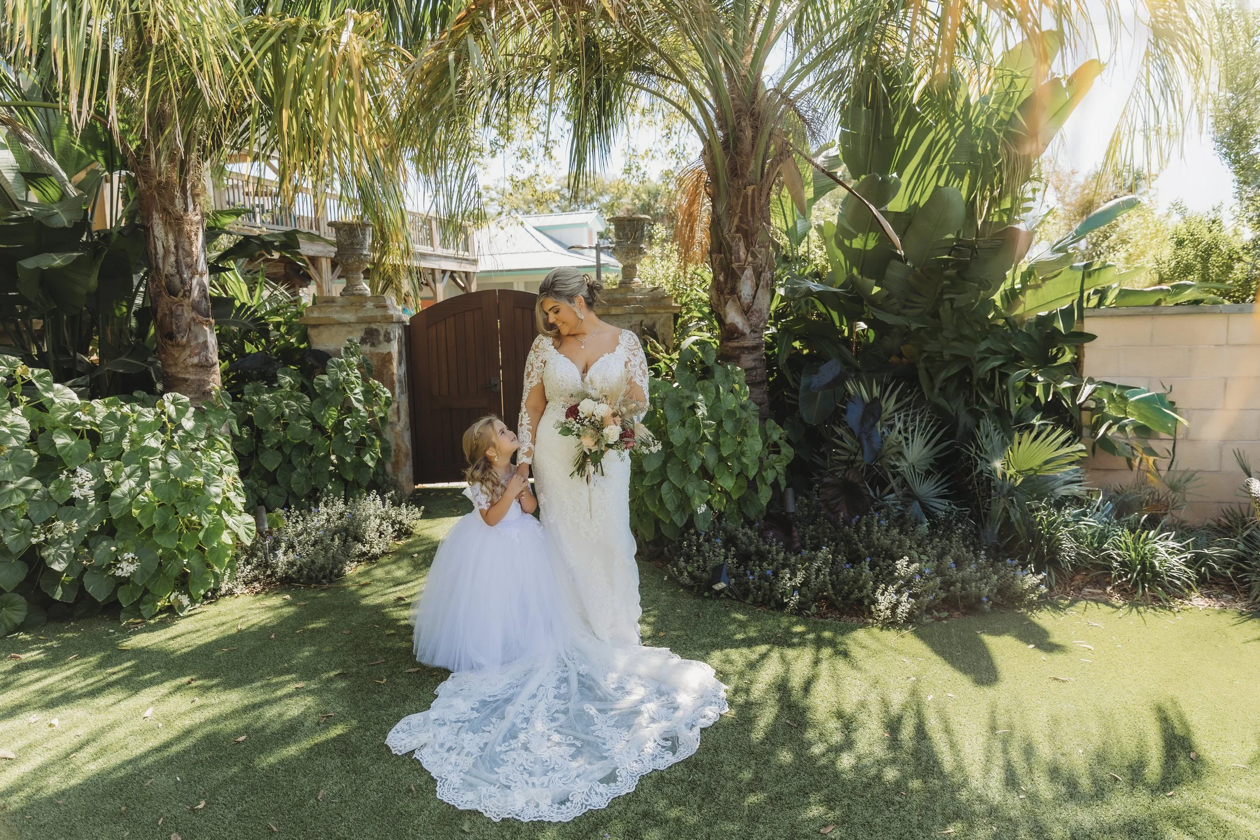 Bride holding her bouquet while sharing a quiet moment with a flower girl in a garden setting.