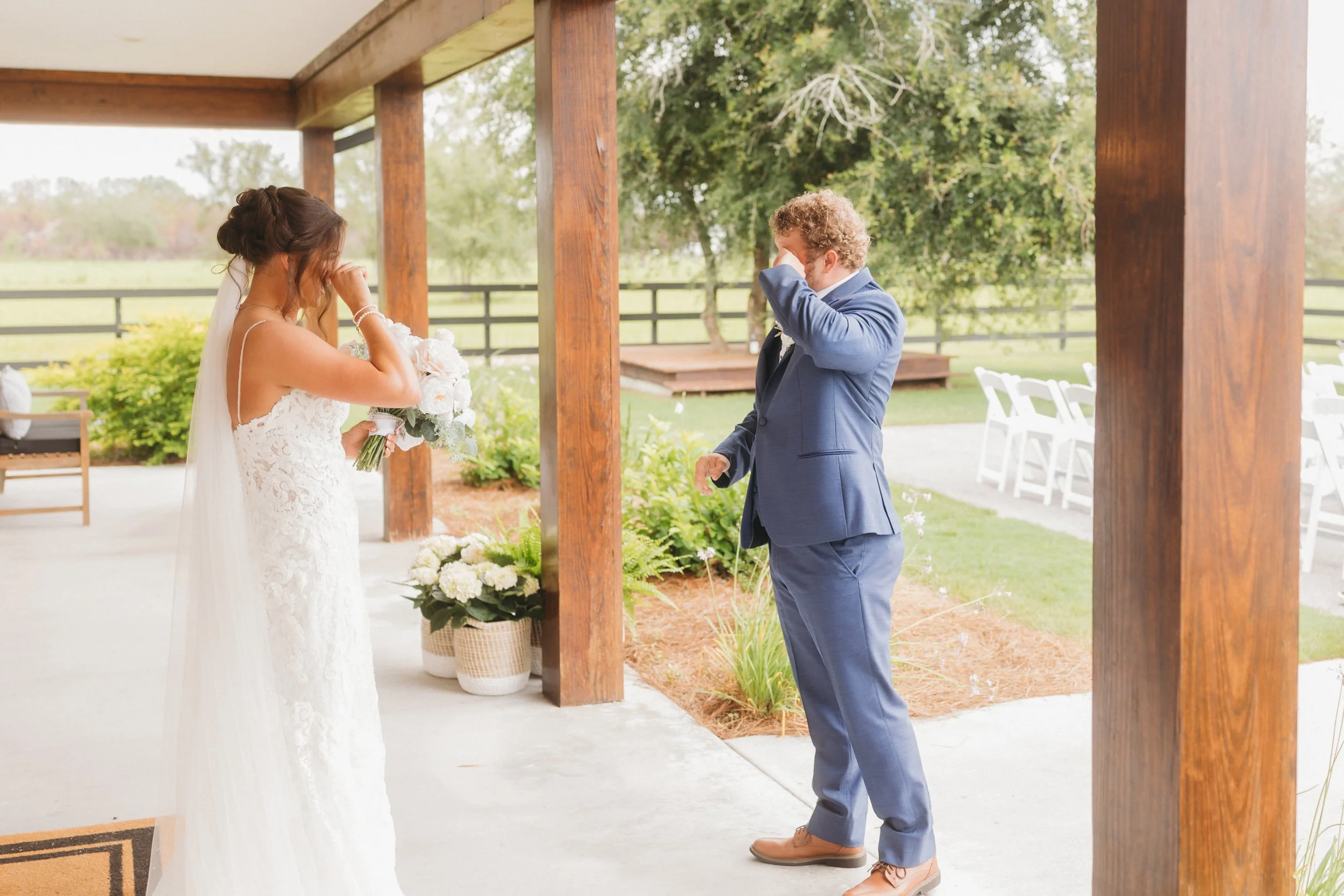 Emma and Dylan embrace between brick pillars as her long veil trails across the lawn beneath a dramatic cloudy sky at Red River Estate.