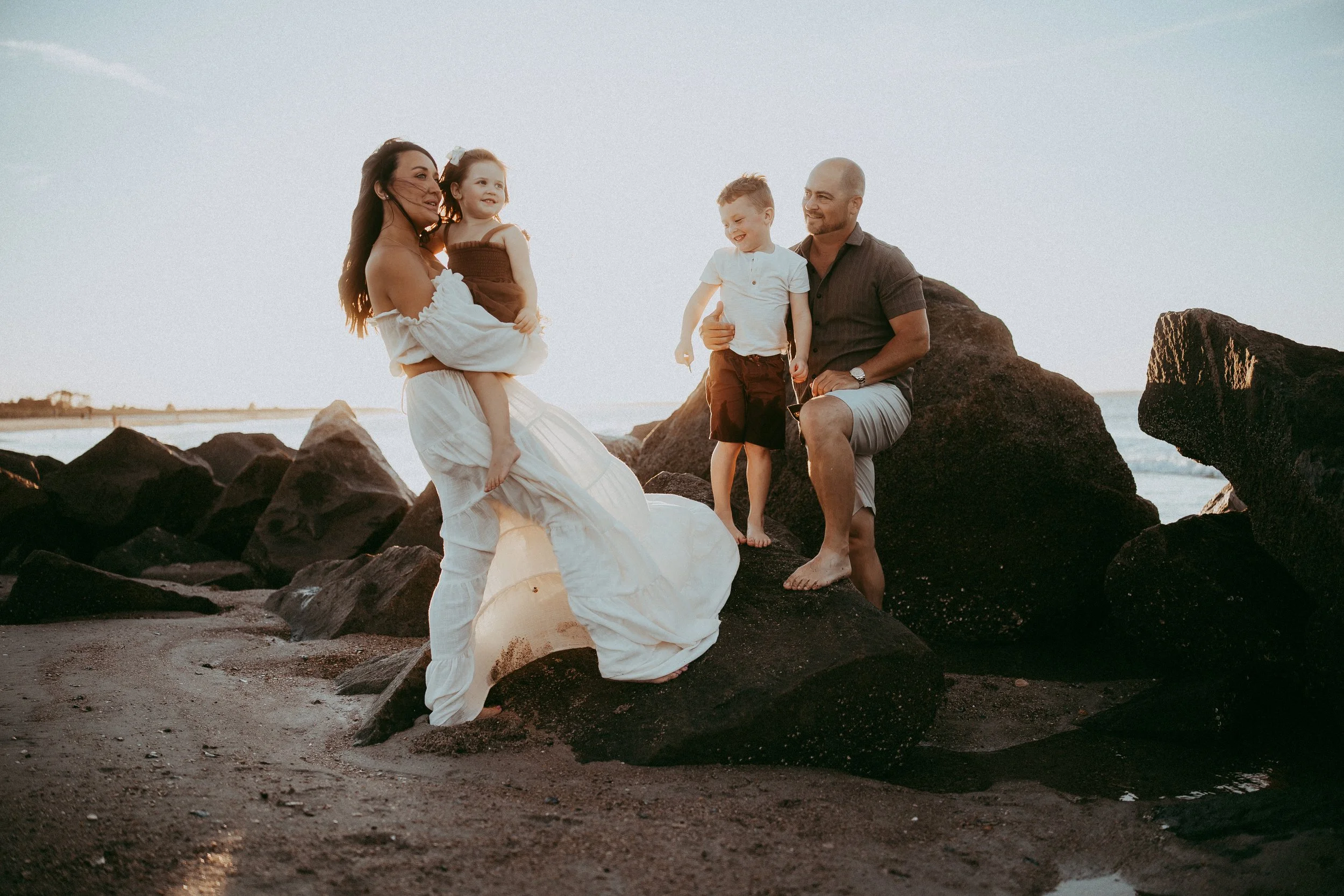 Family of four enjoying a sunset beach portrait session on the rocks, capturing genuine connection, playful moments, and the joy of being together.