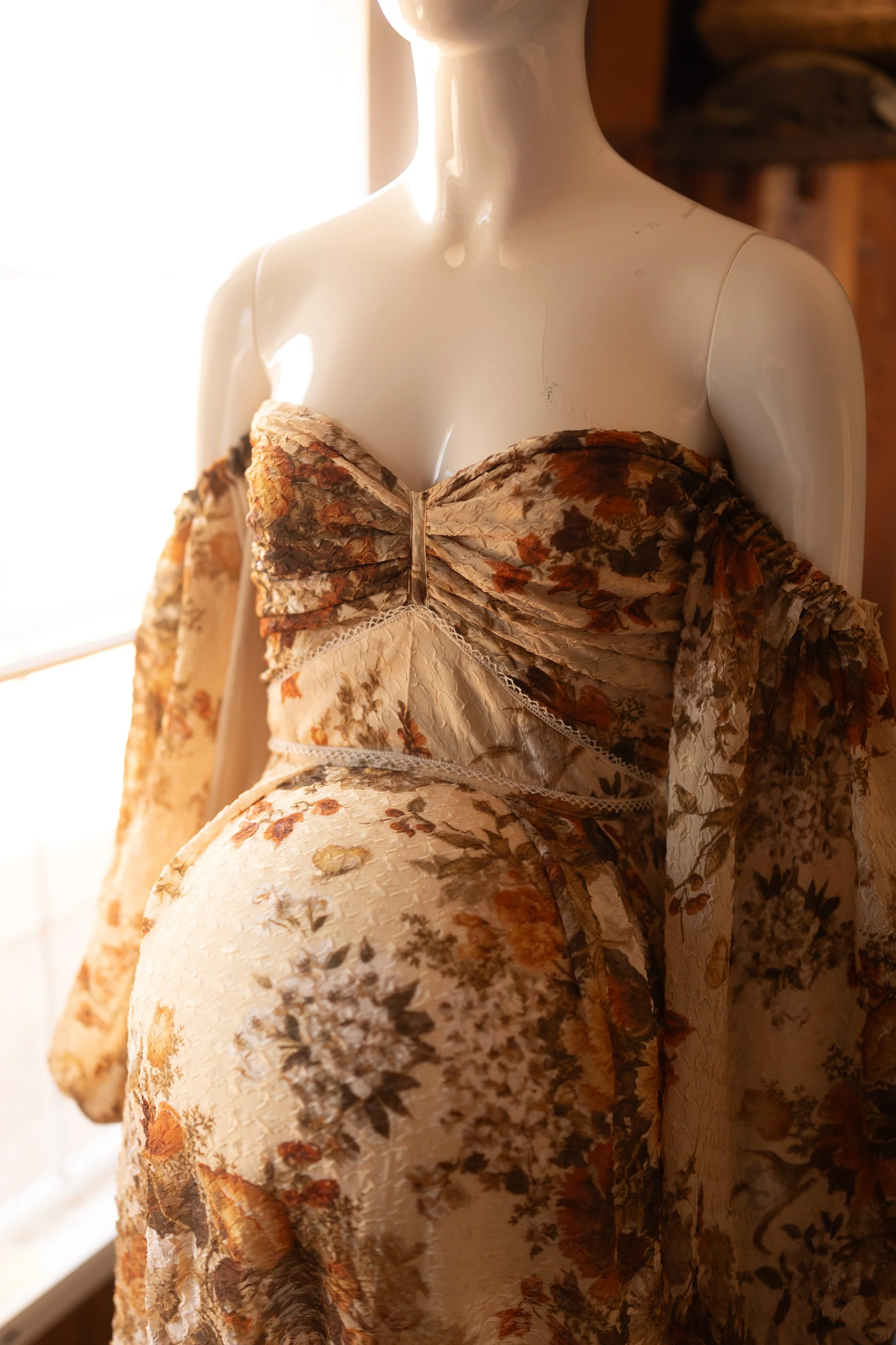 Boho-inspired maternity dress with textured fabric and long flowing sleeves, photographed on a mannequin in warm natural light.