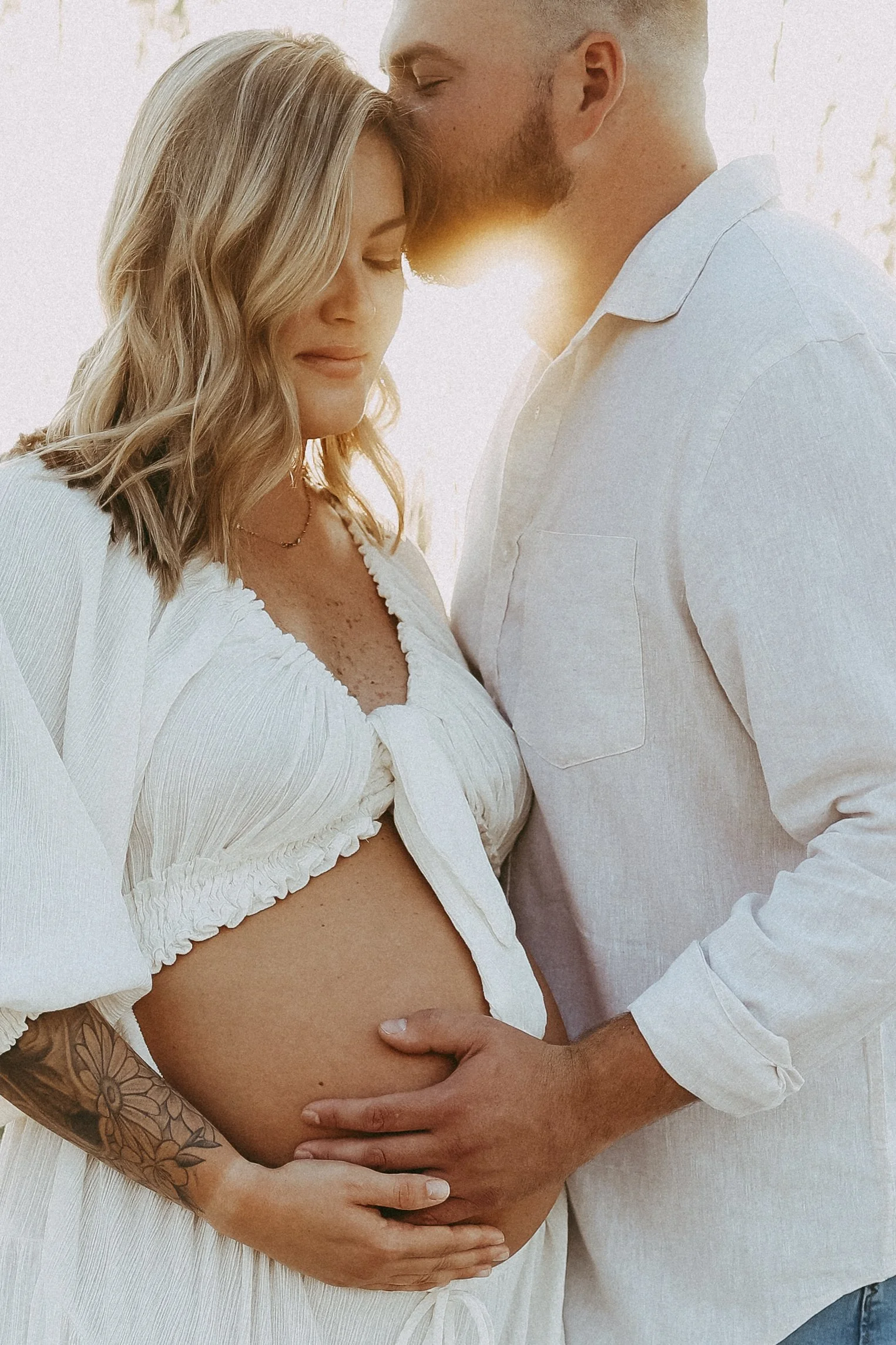 Tender sunset maternity image of an expectant mother and her partner, their hands cradling her belly as the light fades softly around them