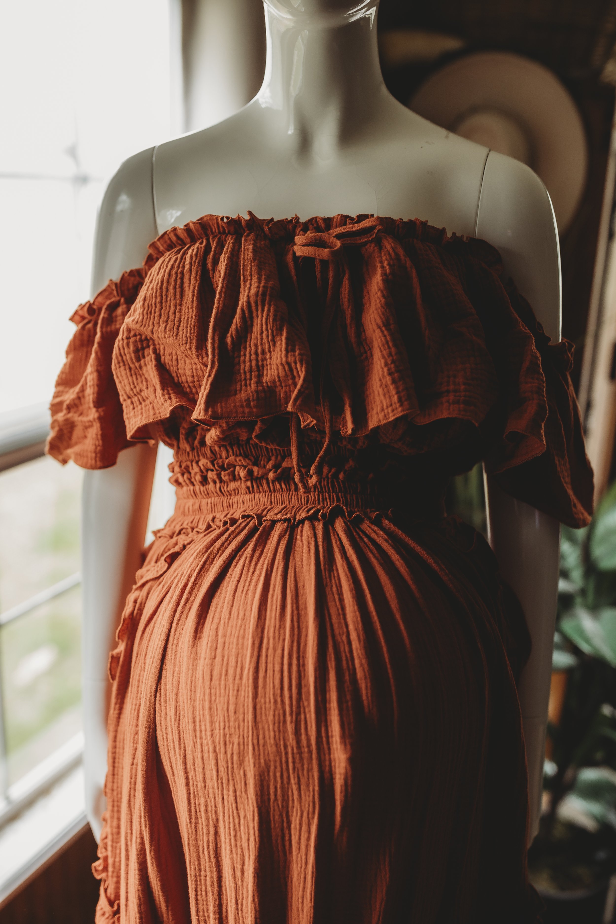 Close-up of an off-the-shoulder rust maternity gown with a ruffled neckline, smocked bodice, and soft crinkled fabric texture.
