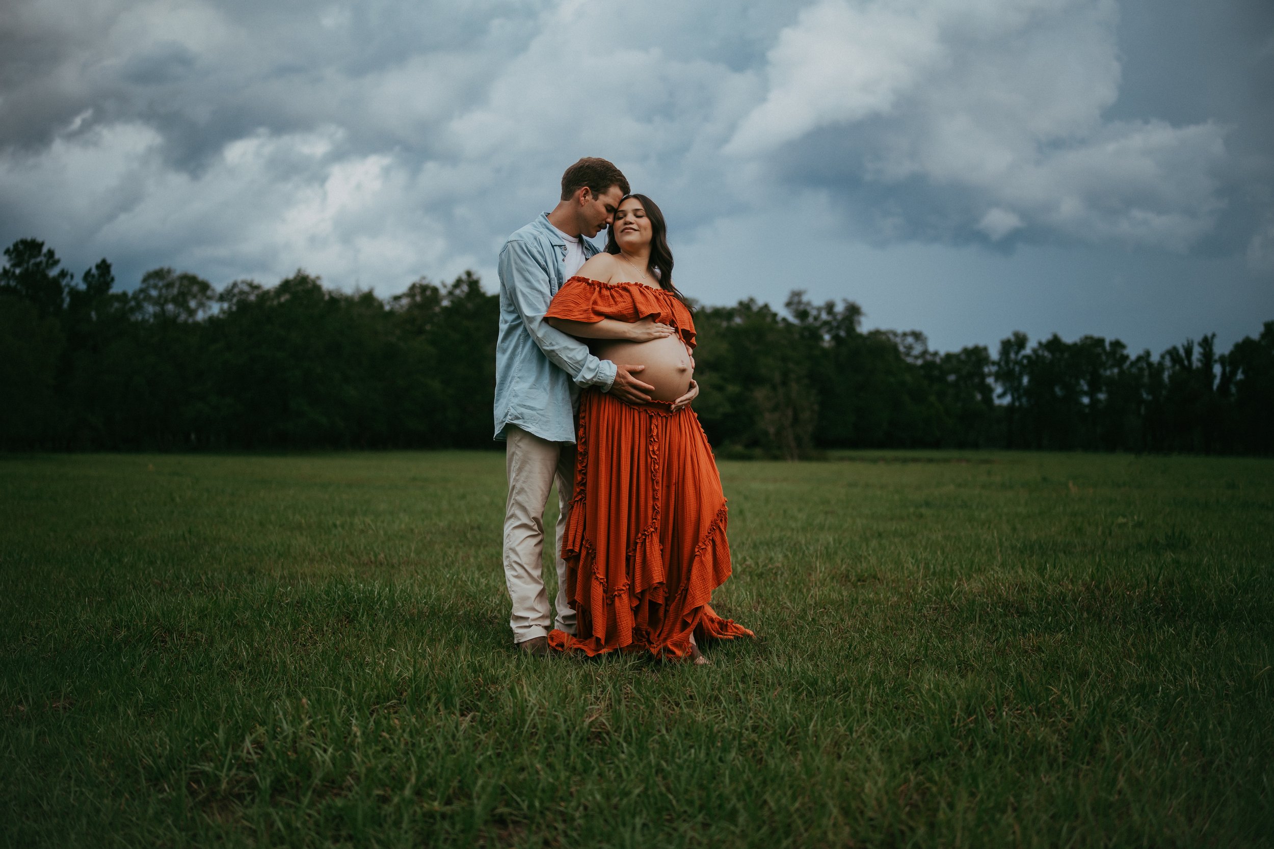Expectant couple embraces beneath dramatic storm clouds during an outdoor maternity session in Hilliard, Florida.