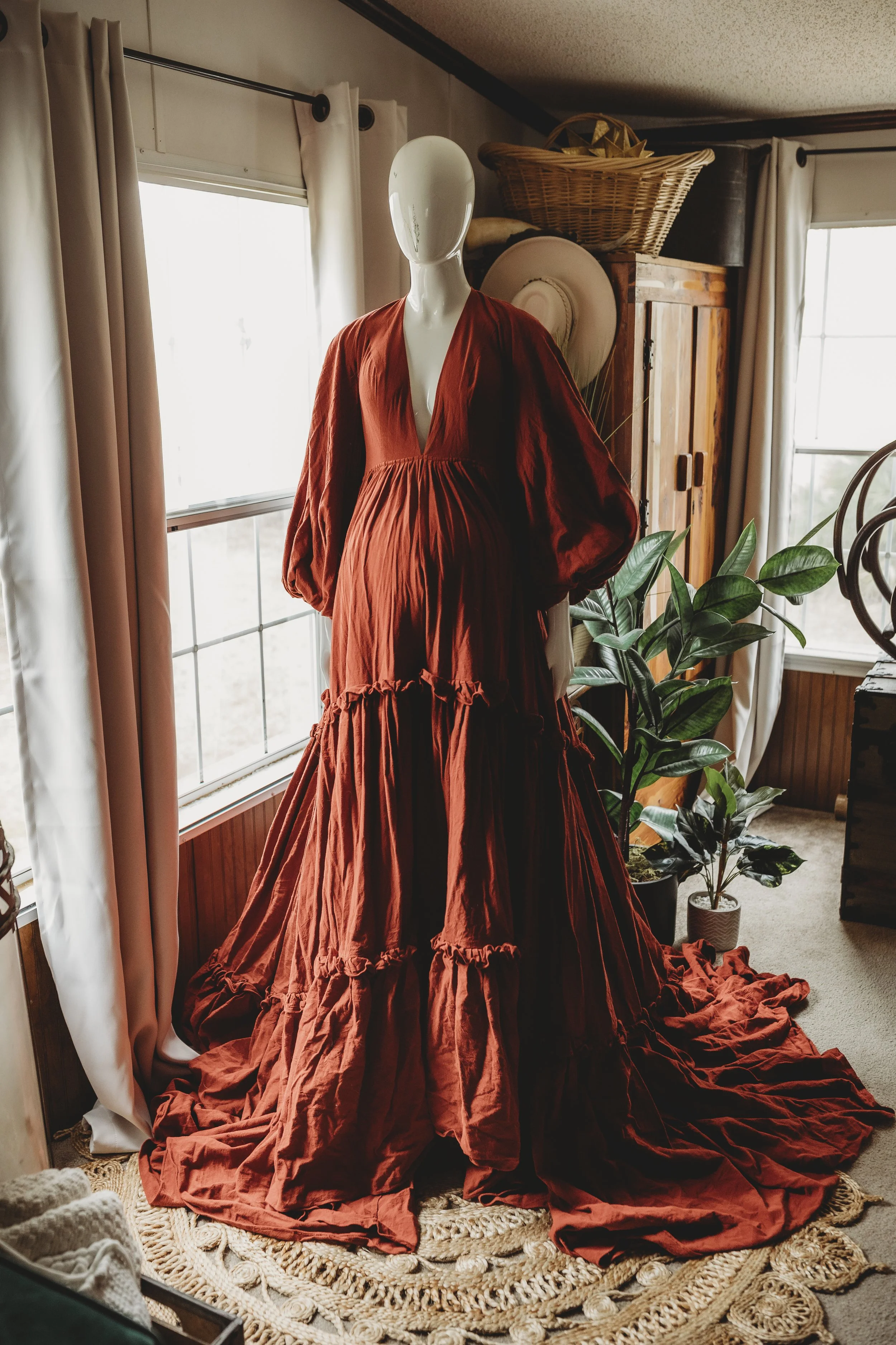 Deep red bohemian maxi dress with a plunging V-neckline, long sleeves, and a flowing tiered skirt, styled on a mannequin in soft natural window light.