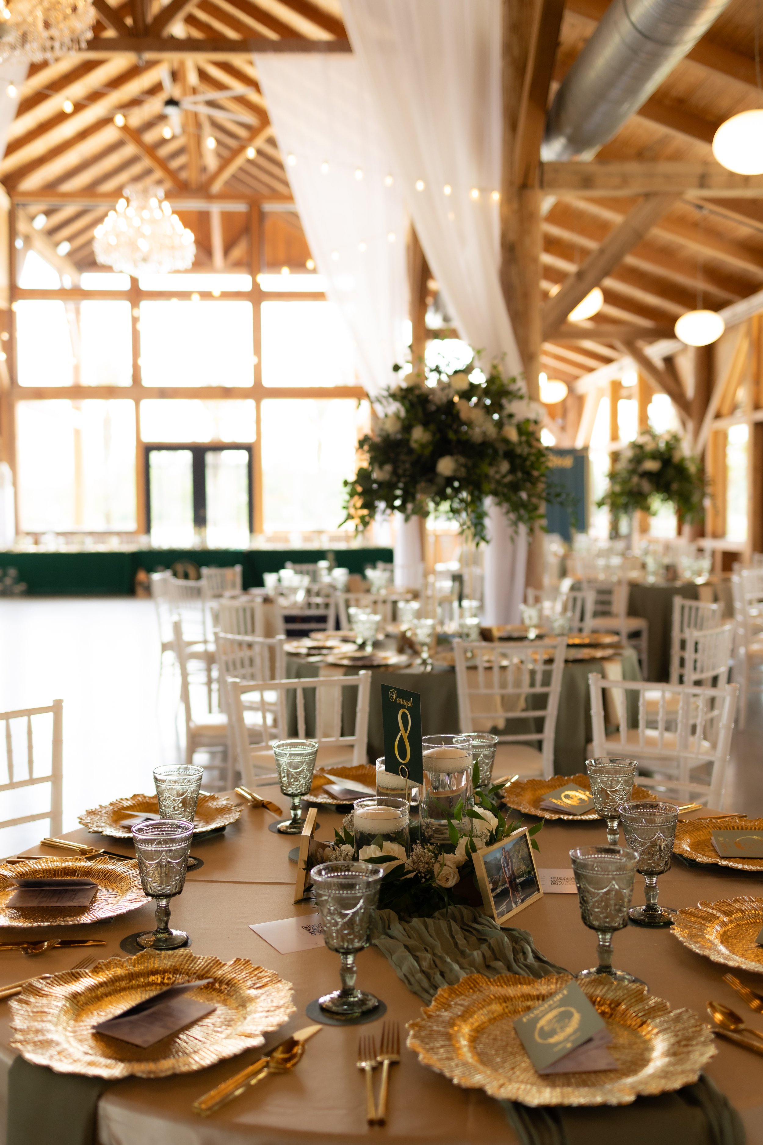 Elegant wedding reception tables decorated with gold place settings, greenery, and candlelit centerpieces.