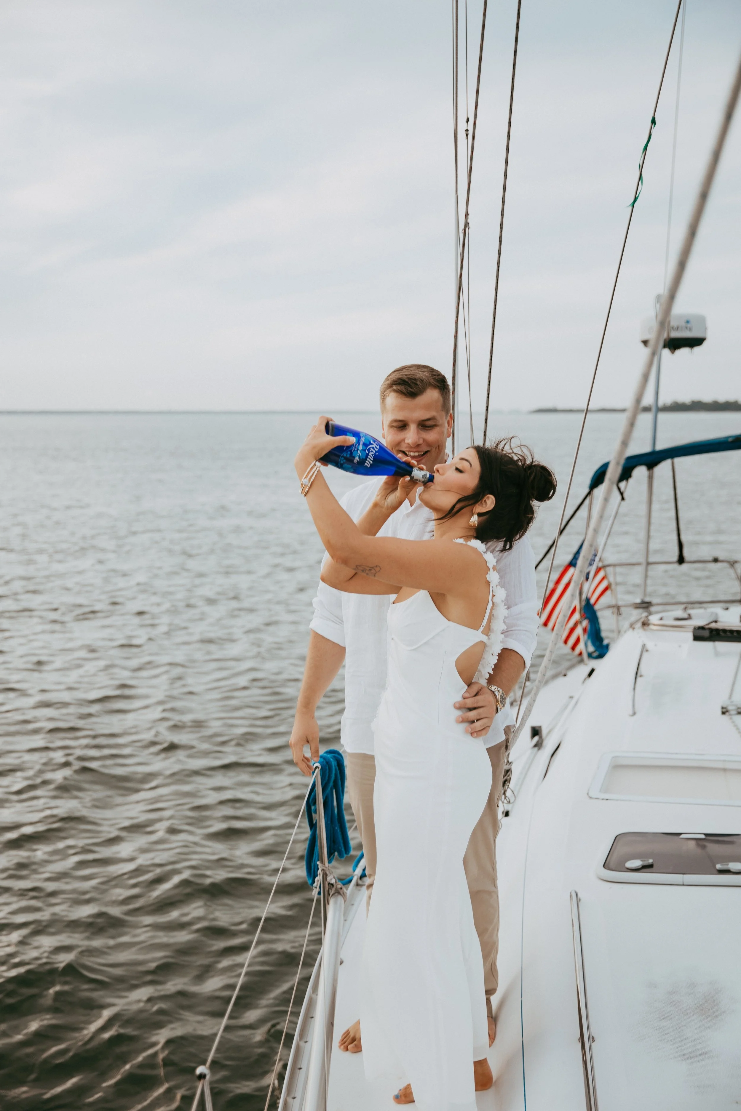 Lyndsey and Adam laugh together with a bottle on the sailboat deck.